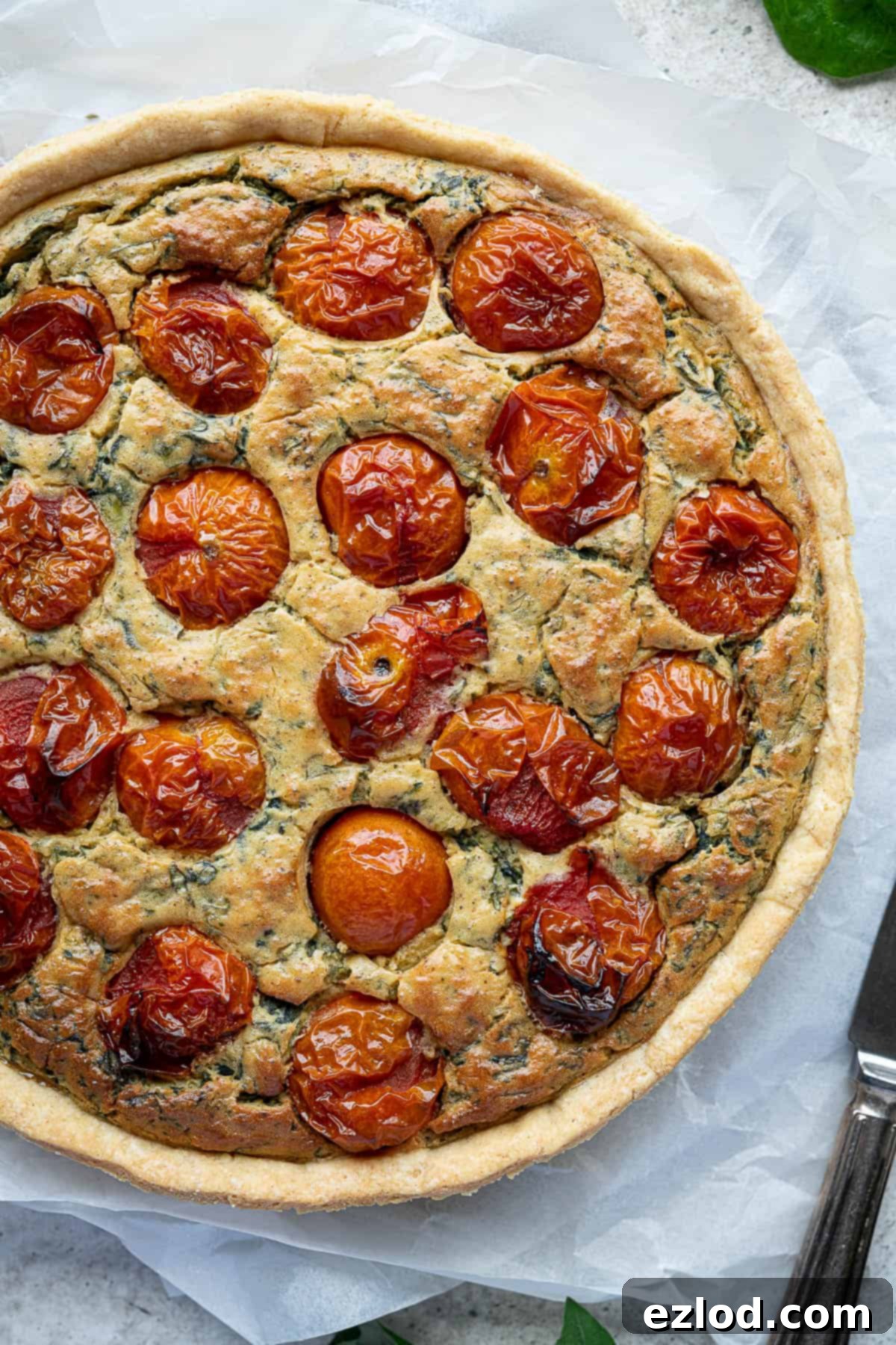 A close-up of the golden-brown, freshly baked vegan tomato spinach quiche, looking perfectly set.