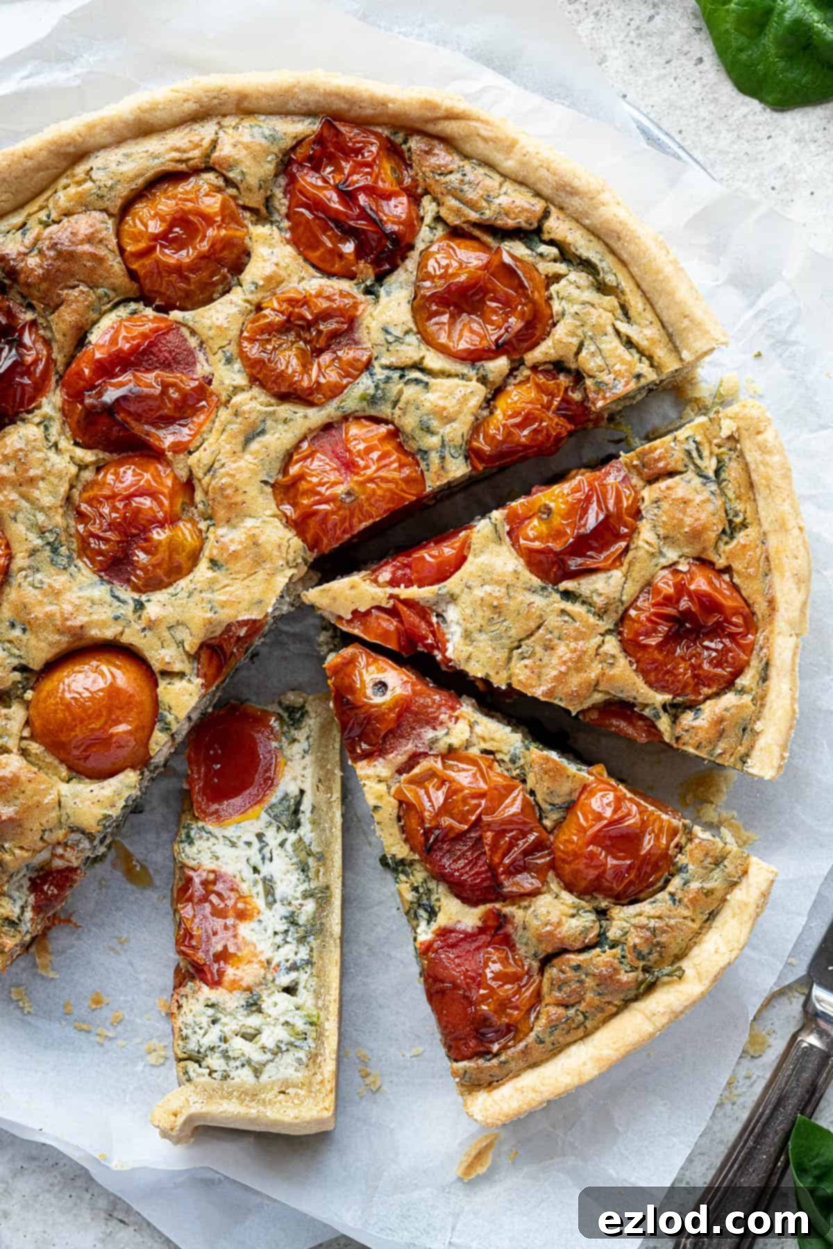 A close-up of a perfectly sliced vegan tomato spinach quiche, with one slice tilted on its side, revealing the creamy filling.