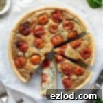 The sliced vegan tomato spinach quiche on a sheet of baking parchment surrounded by fresh basil, spinach and tomatoes.