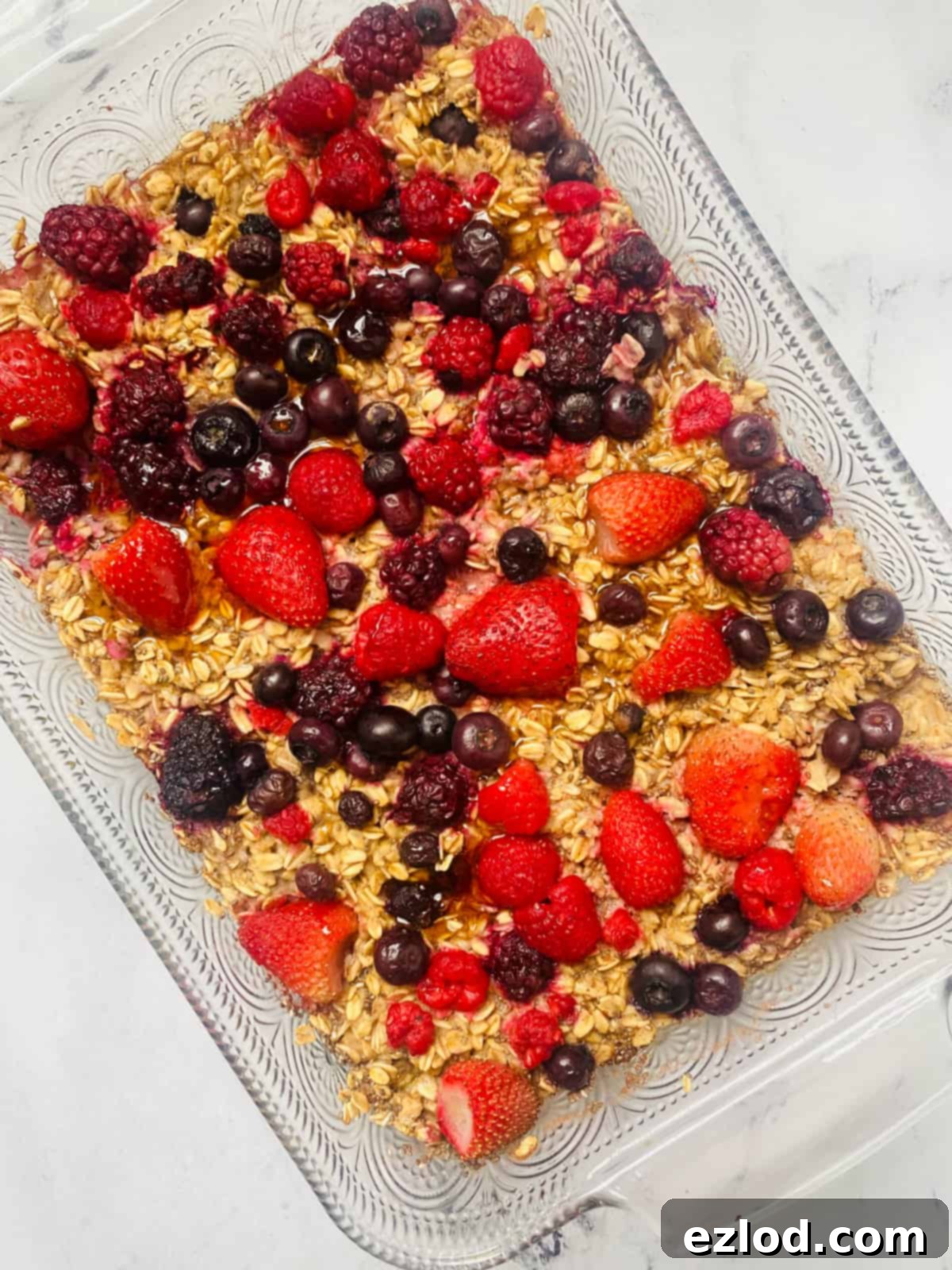 A beautiful baking dish of golden baked oats, freshly pulled from the oven, generously topped with glistening frozen berries, ready to be served. 