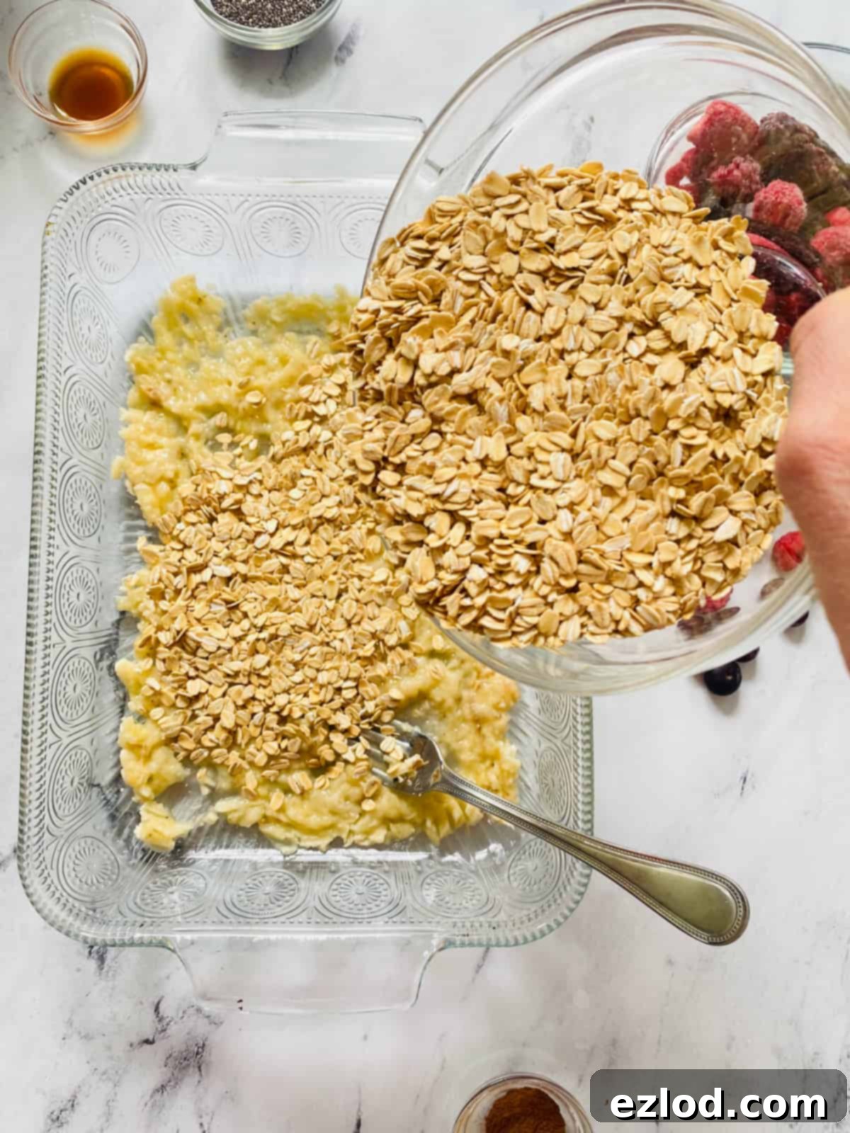 Dry ingredients, including rolled oats and chia seeds, being added directly into the baking dish with mashed bananas. 