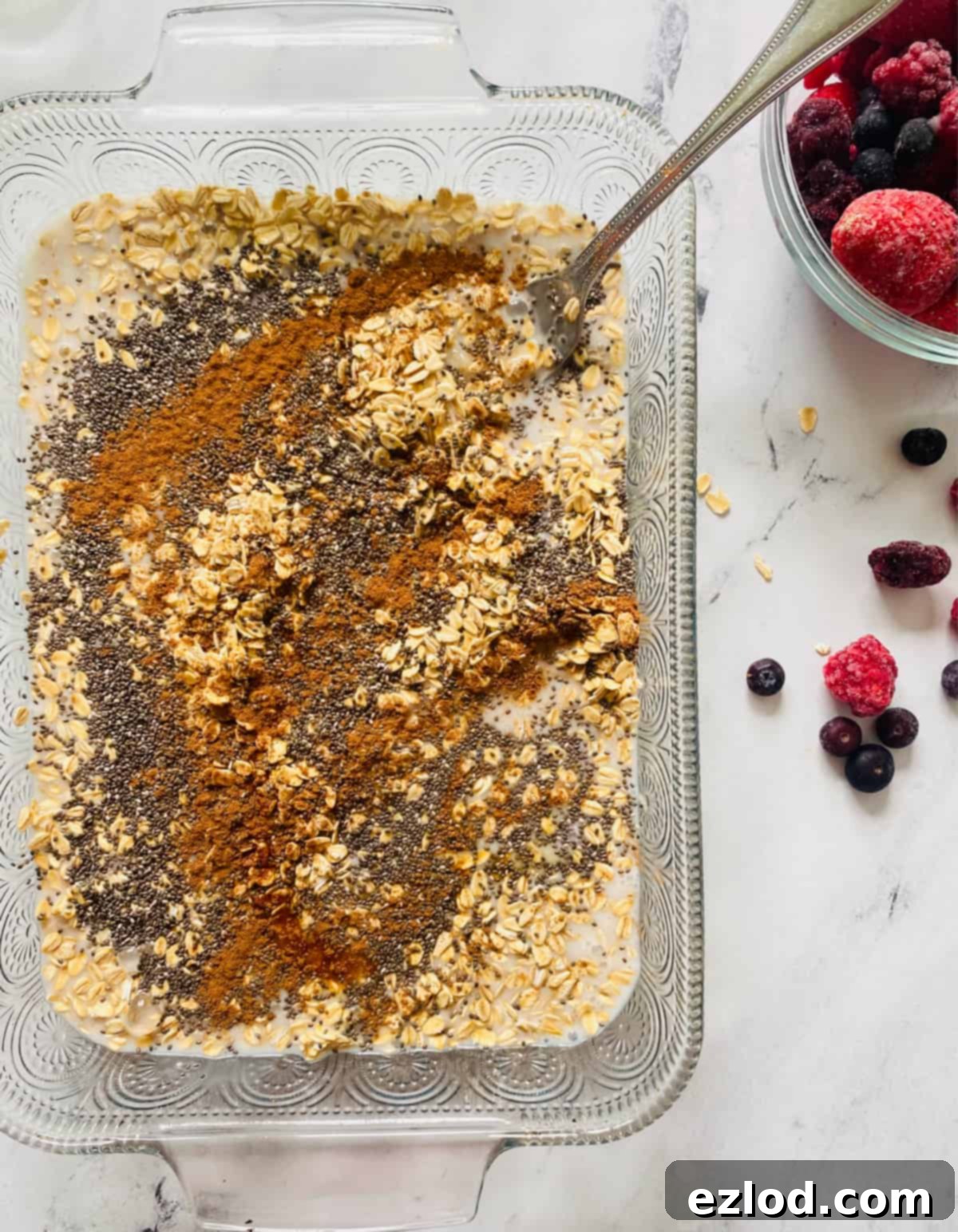 Unsweetened almond milk and vanilla extract being poured over the mixture of mashed bananas, oats, and seeds in the baking dish. 