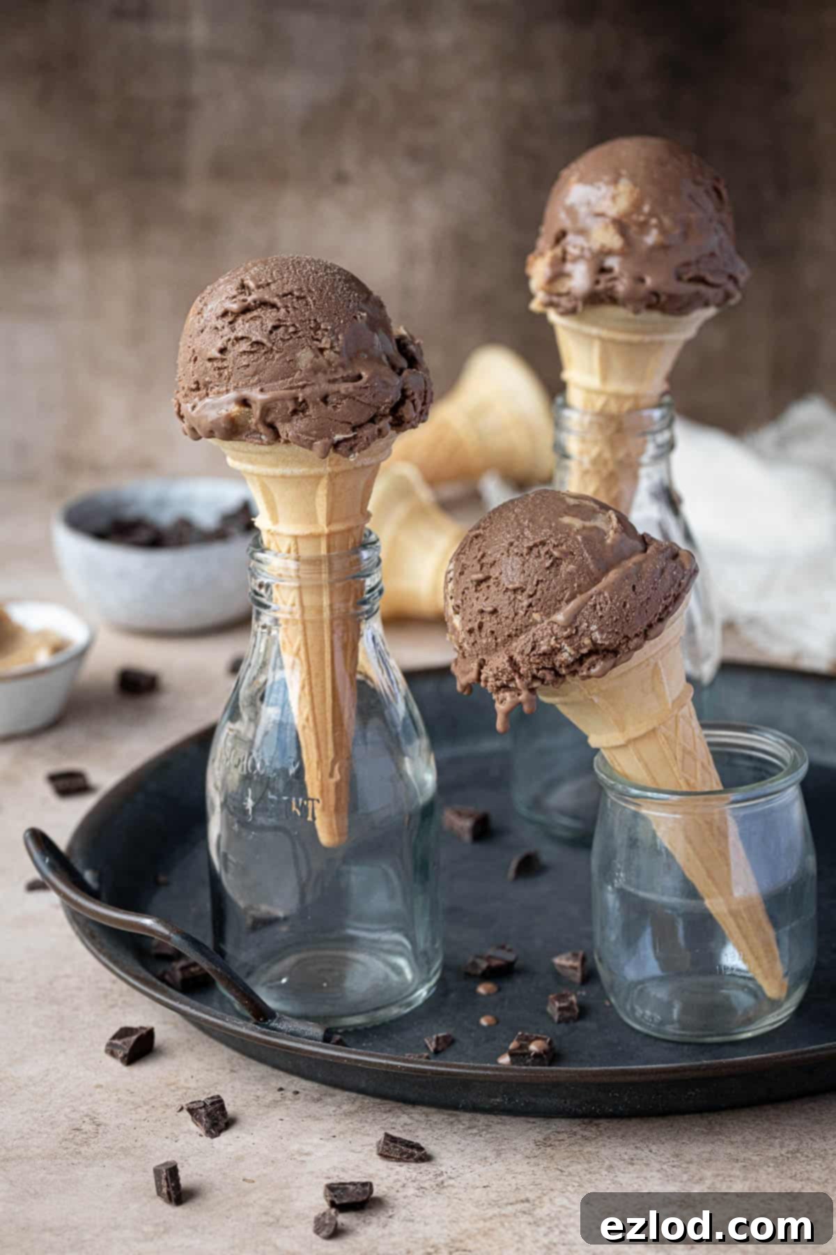 Three cones of chocolate peanut butter ice cream in glass bottles on a metal tray.