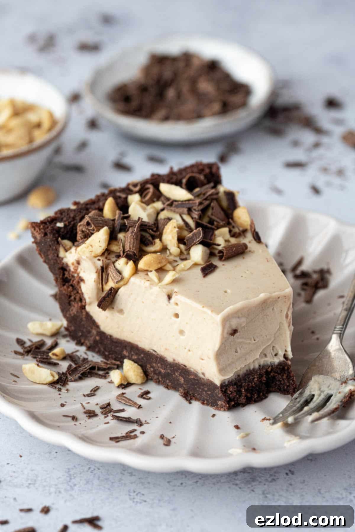 A vibrant close-up shot of a single slice of vegan peanut butter pie, highlighting the distinct layers of chocolate crust and rich, creamy peanut butter filling, garnished with a few scattered peanuts.