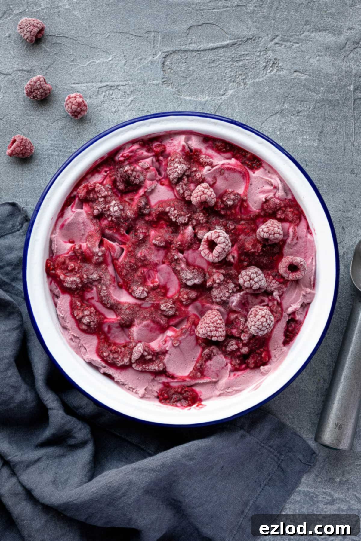 Vegan raspberry ice cream in a pie dish, garnished with frozen raspberries and a grey cloth.