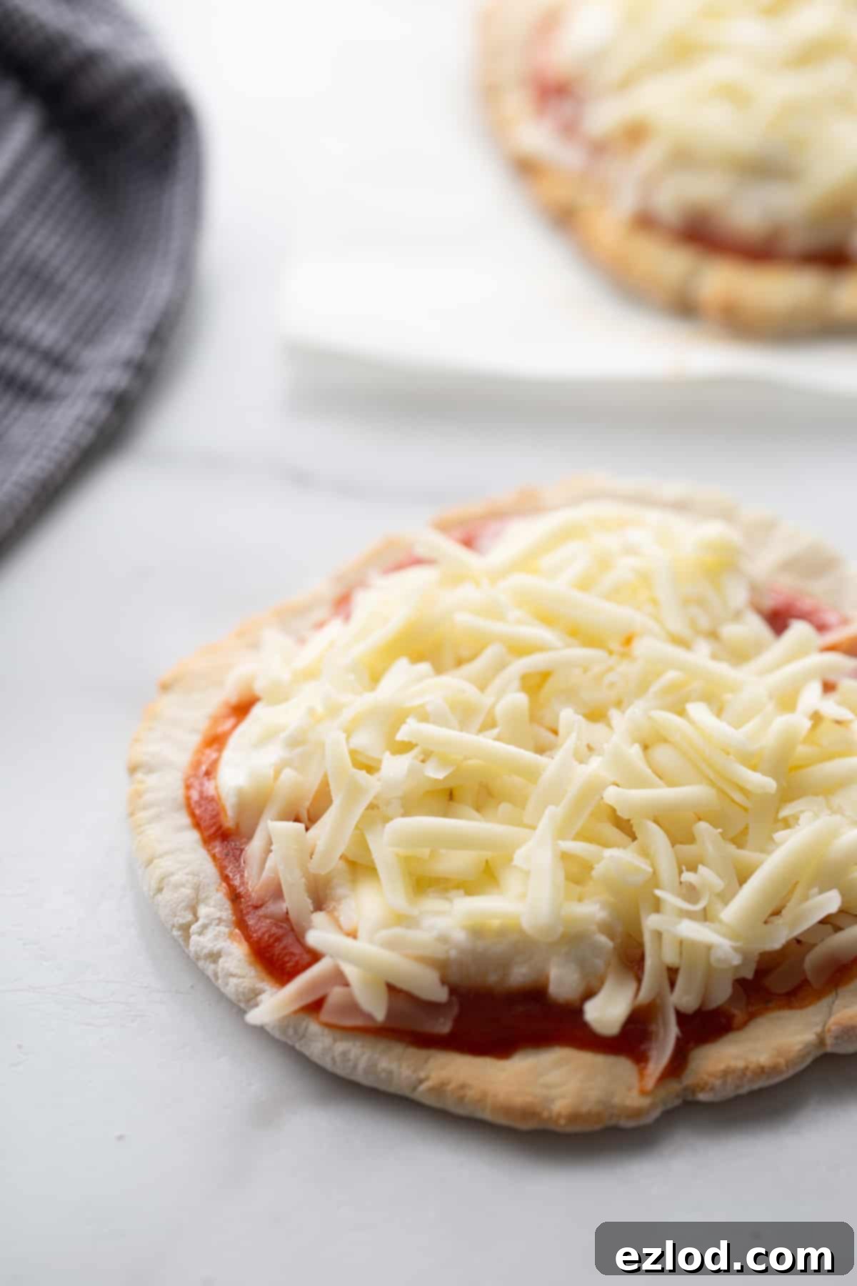 A small personal gluten-free Greek yogurt pizza, topped with sauce, creamy ricotta, and melted mozzarella cheese, rests on a pristine white kitchen counter.