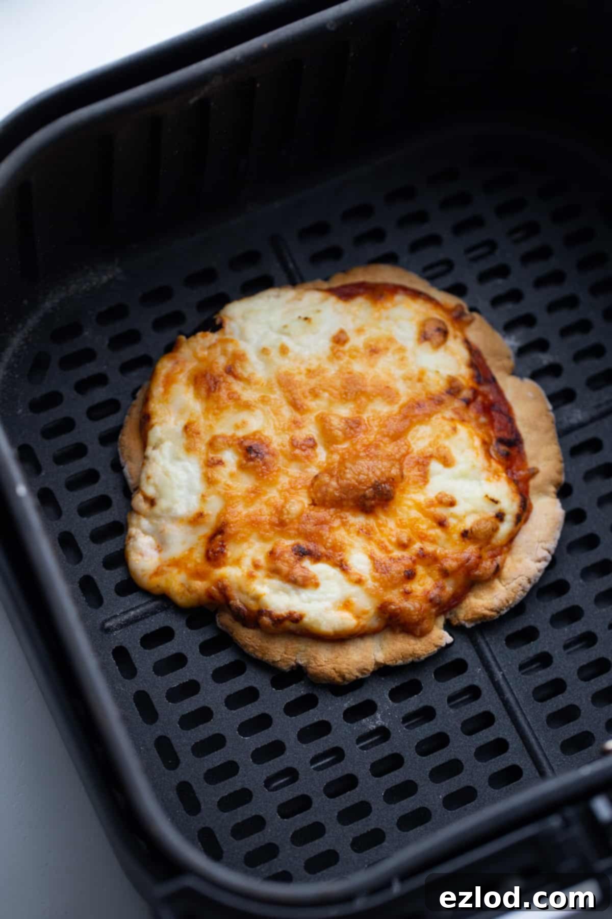 A small personal gluten-free pizza, featuring perfectly melted and crispy cheese, sits invitingly inside an air fryer basket.