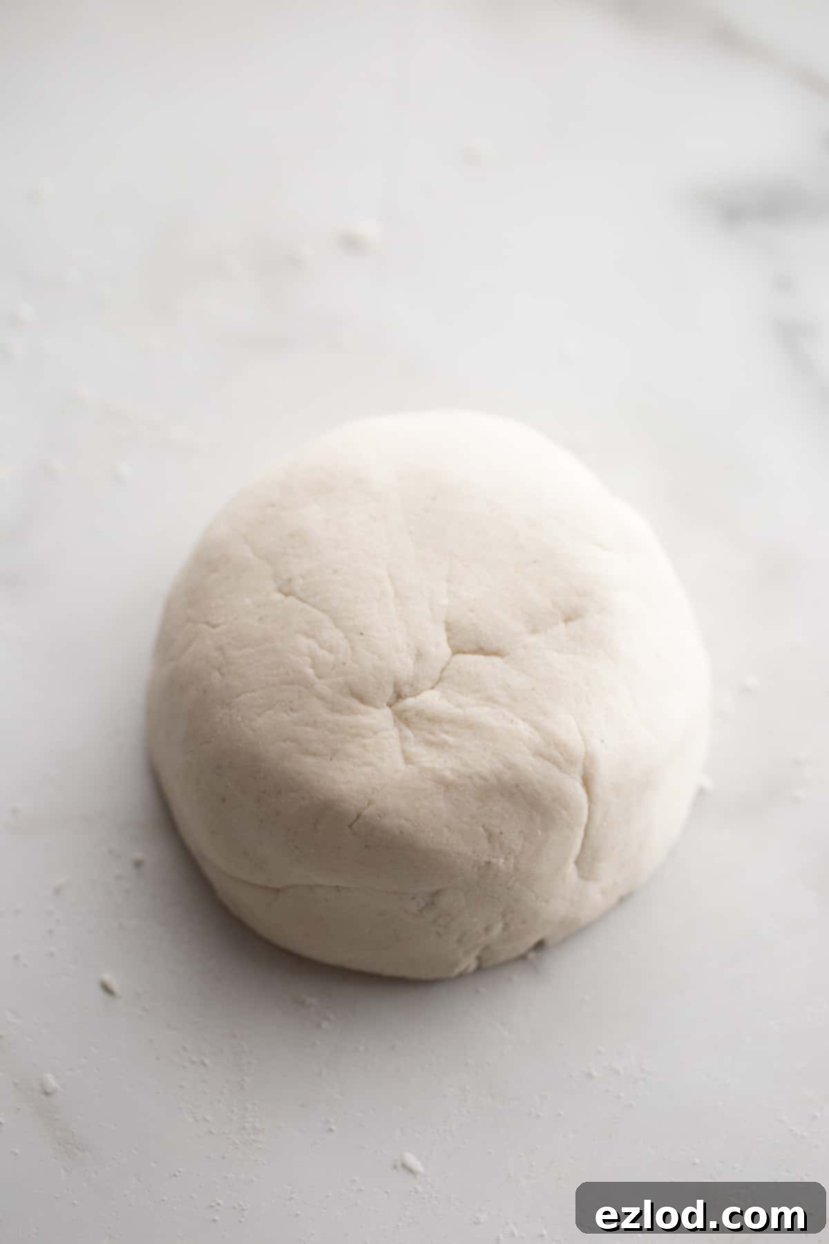 Smooth, kneaded gluten-free pizza dough resting on a white countertop, ready to be divided and rolled.