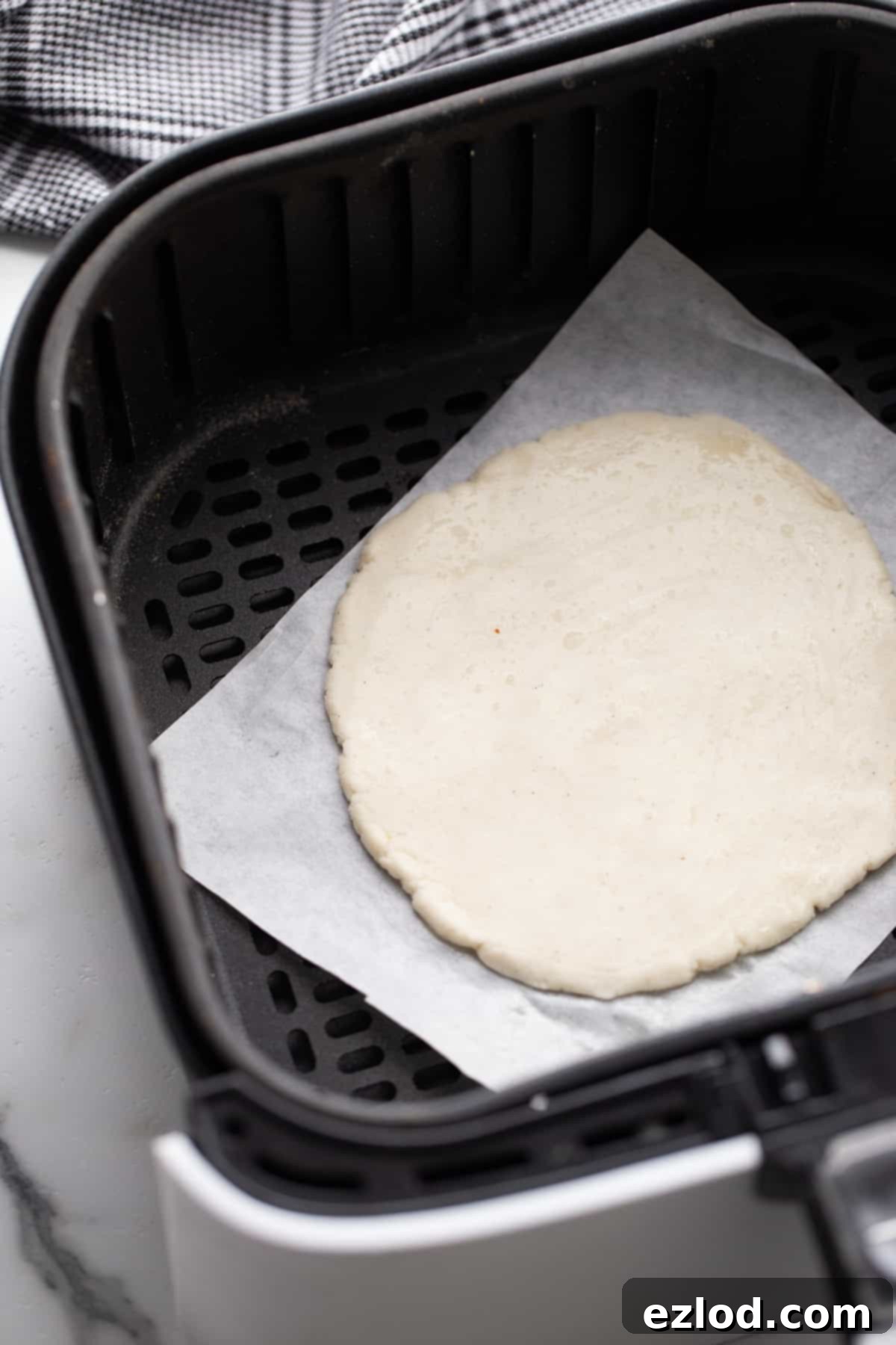 A perfectly rolled out gluten-free pizza crust, ready for toppings, placed on parchment paper inside an air fryer basket.