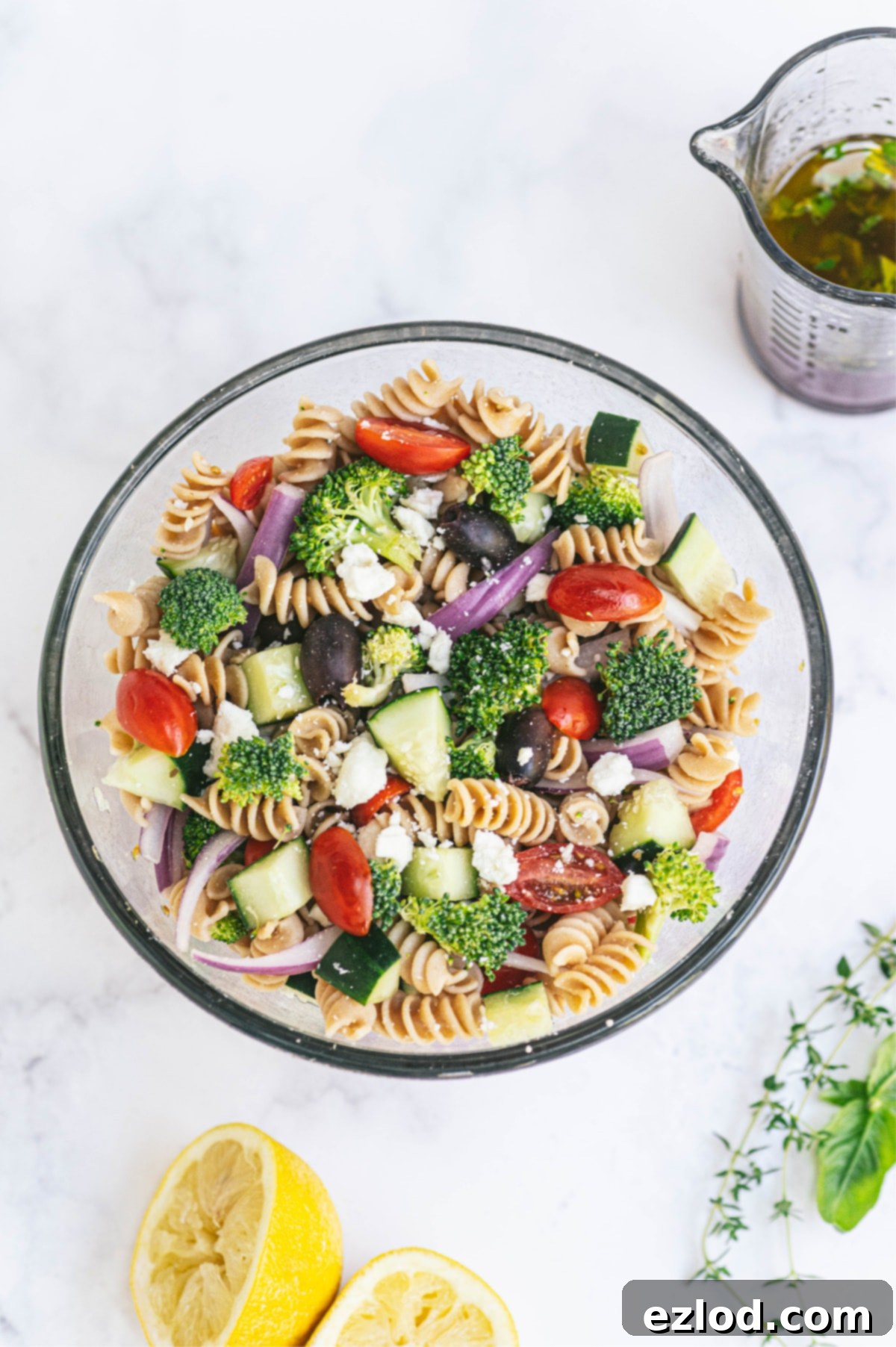 A large bowl of pasta veggie salad with dressing on the side.