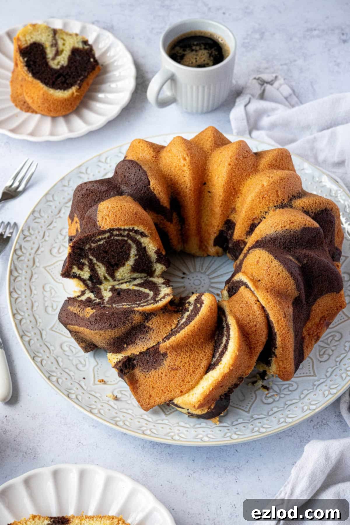 Chocolate orange bundt cake on a white plate with plates of cake and a cup of coffee.