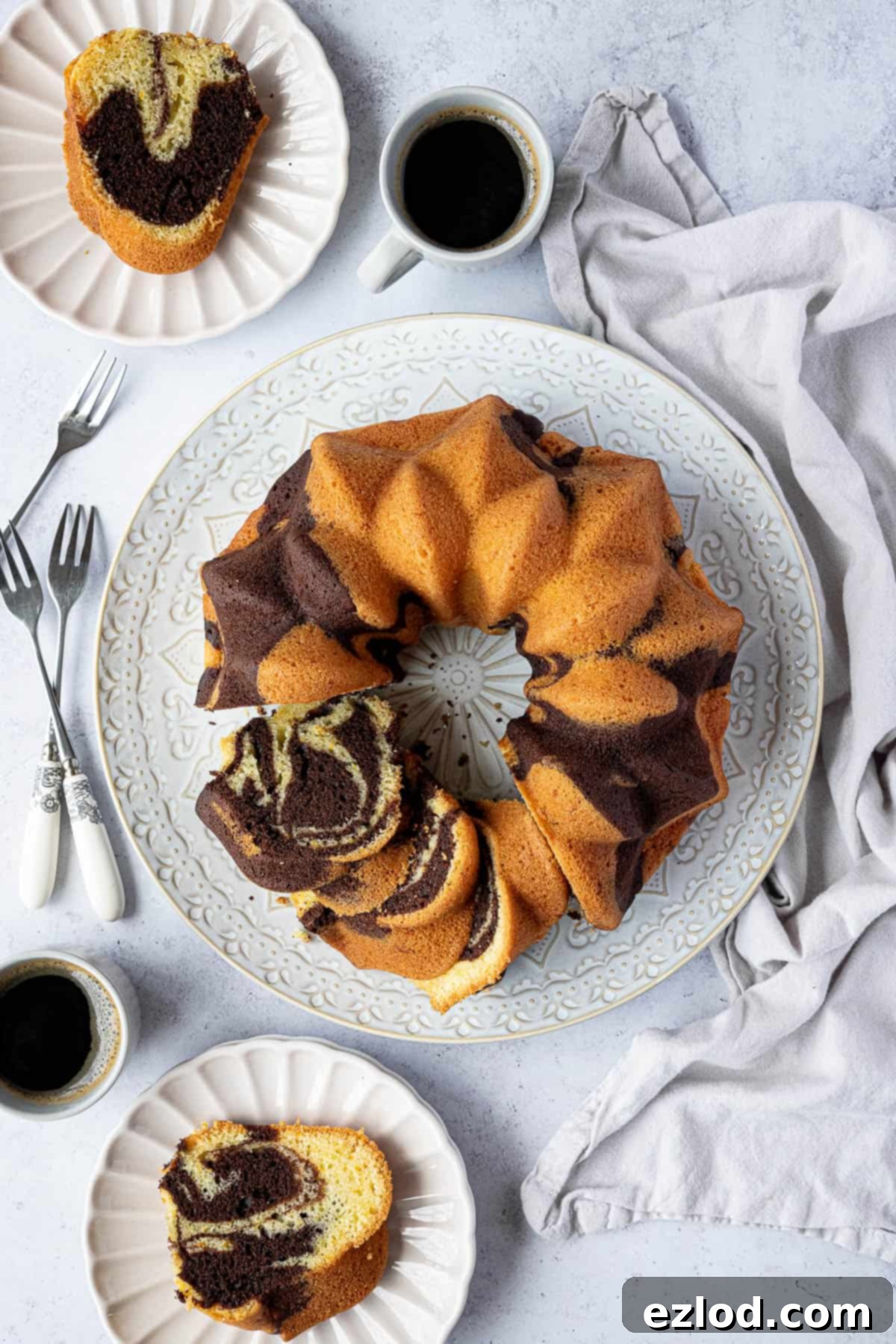 Chocolate orange bundt cake on a white plate with plates of cake and cups of coffee.