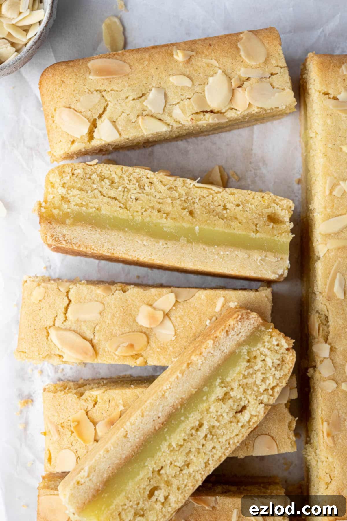 Zesty Vegan Bakewell Bliss 2 Lemon Bakewell slices on a sheet of baking parchment, showcasing their golden-brown edges and layered texture.