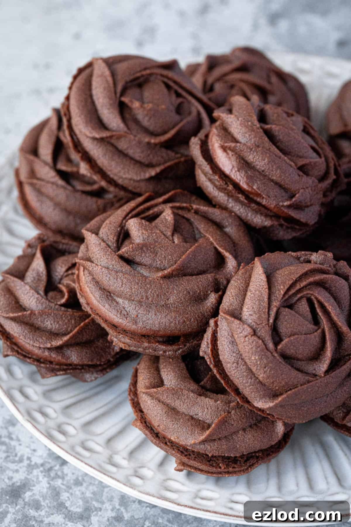 Close up of a pile of chocolate Viennese whirl biscuits on a white plate.