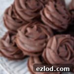 Close up of a pile of chocolate Viennese whirl biscuits on a white plate.