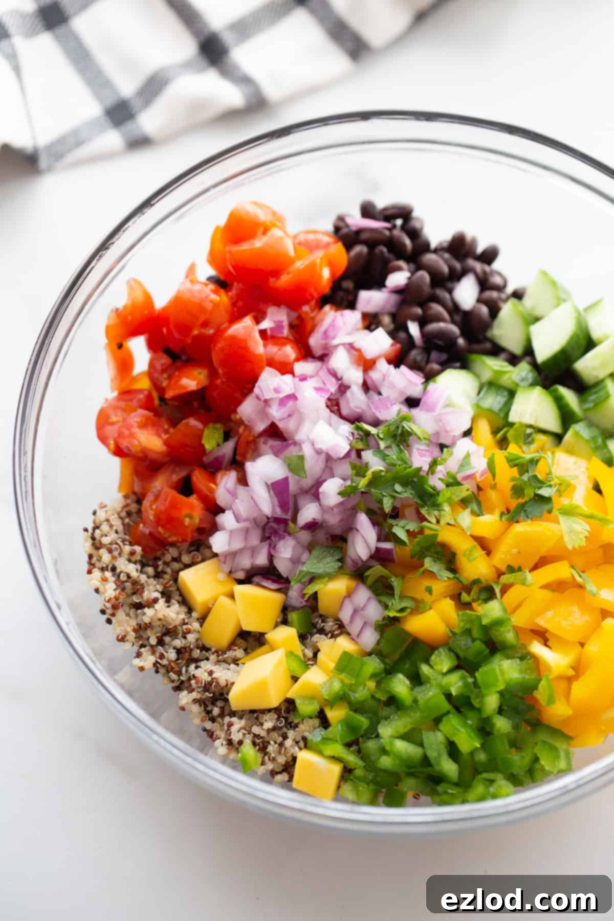 Chopped veggies, black beans, and cooked quinoa in a glass bowl, ready to be mixed.