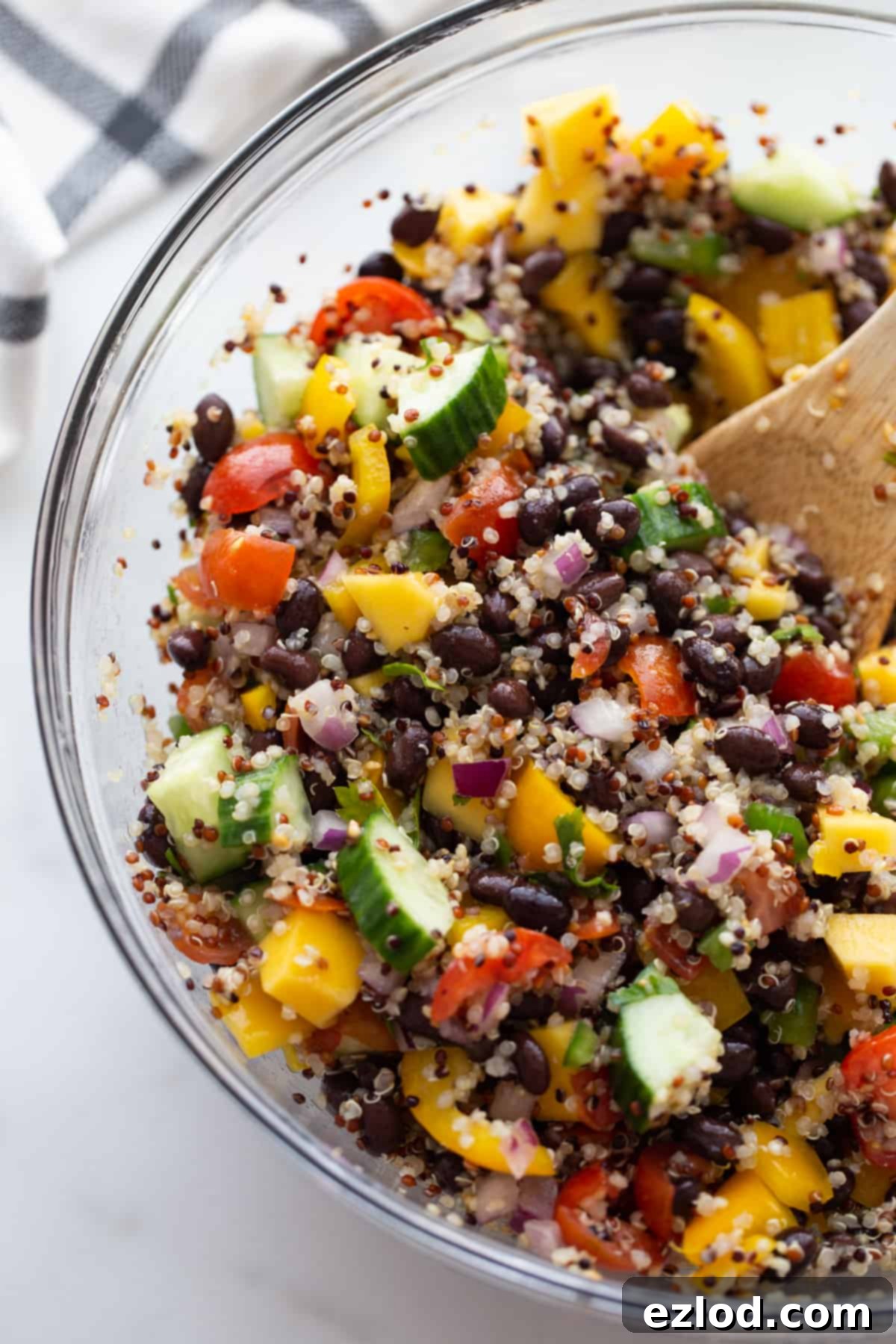 Chopped veggies, black beans, mangoes, and cooked quinoa in a bowl all mixed together, showcasing the finished salad.