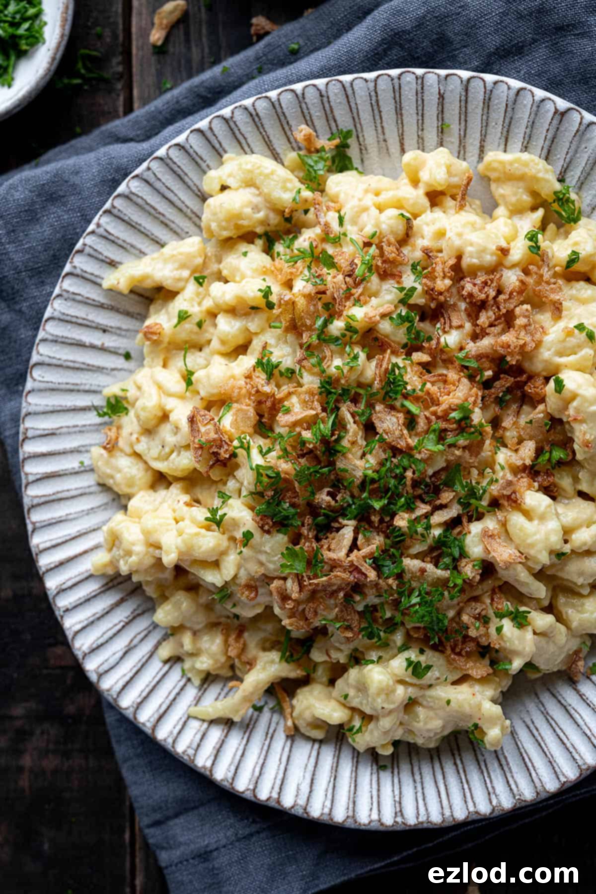 Close up of a plate of vegan spaetzle with cheese sauce and crispy fried onions.