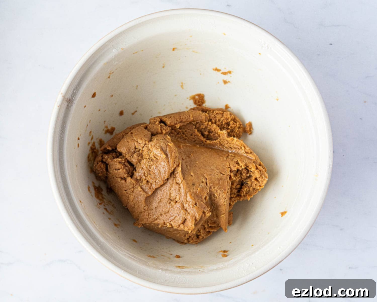 The smooth, orange-tinted dough for vegan pumpkin biscotti in a mixing bowl.