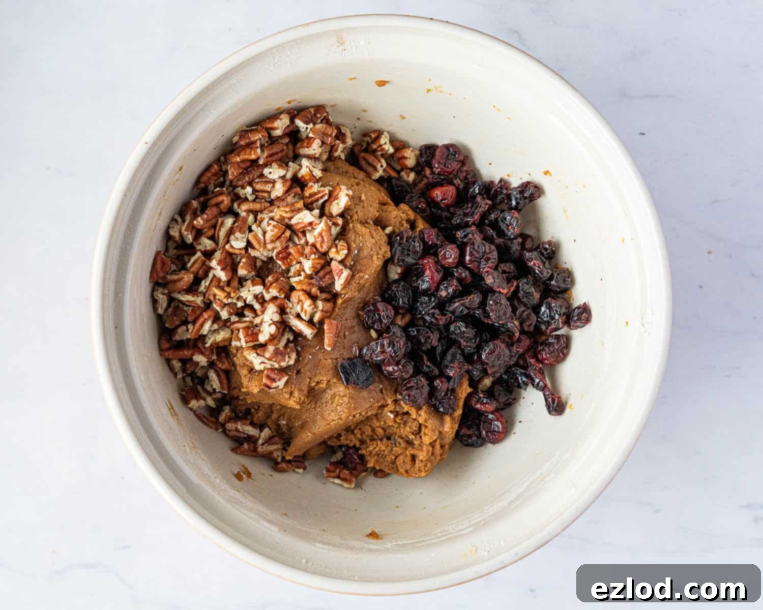 Pecans and cranberries being added to the vegan pumpkin biscotti dough.