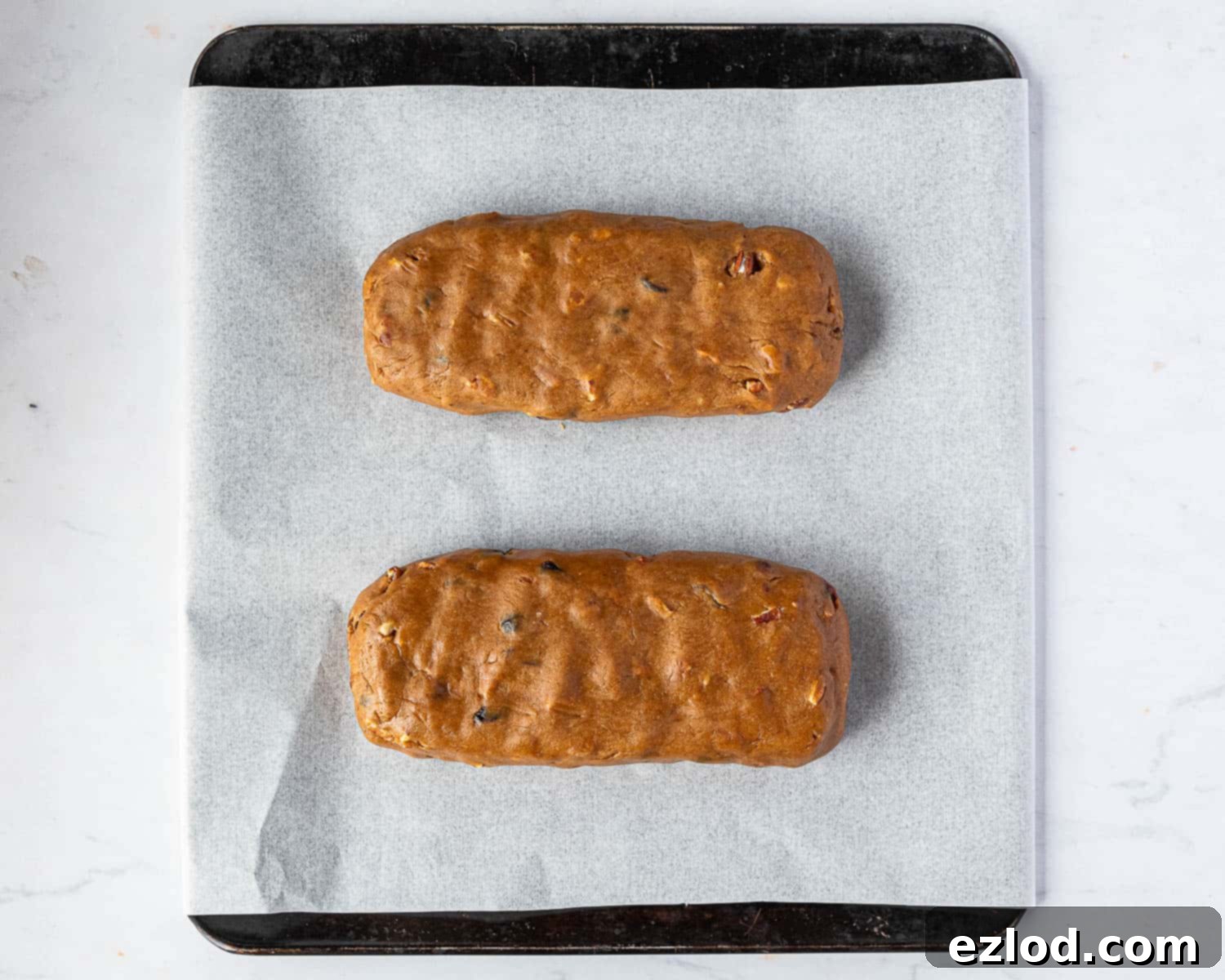 Two shaped logs of vegan pumpkin biscotti dough on a parchment-lined baking sheet, ready for the first bake.