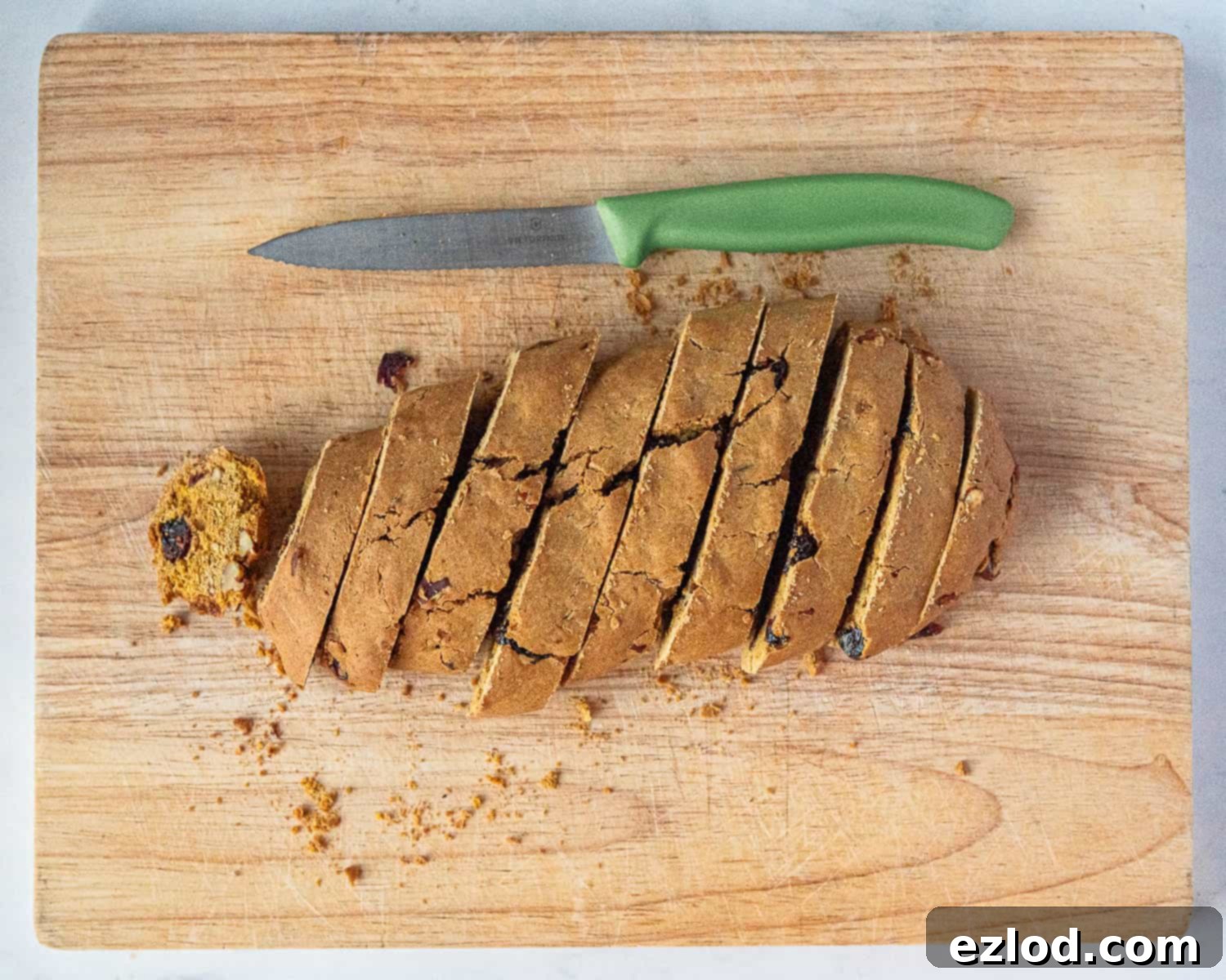A baked biscotti log partially sliced into diagonal pieces with a serrated knife.