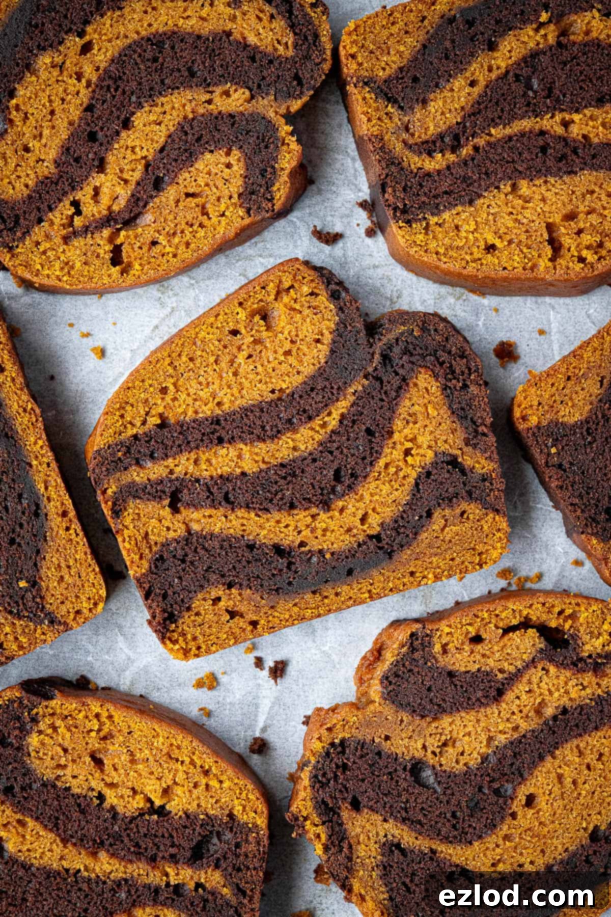 Slices of fluffy vegan pumpkin chocolate marble bread arranged neatly on a sheet of baking parchment, showcasing the beautiful swirl.