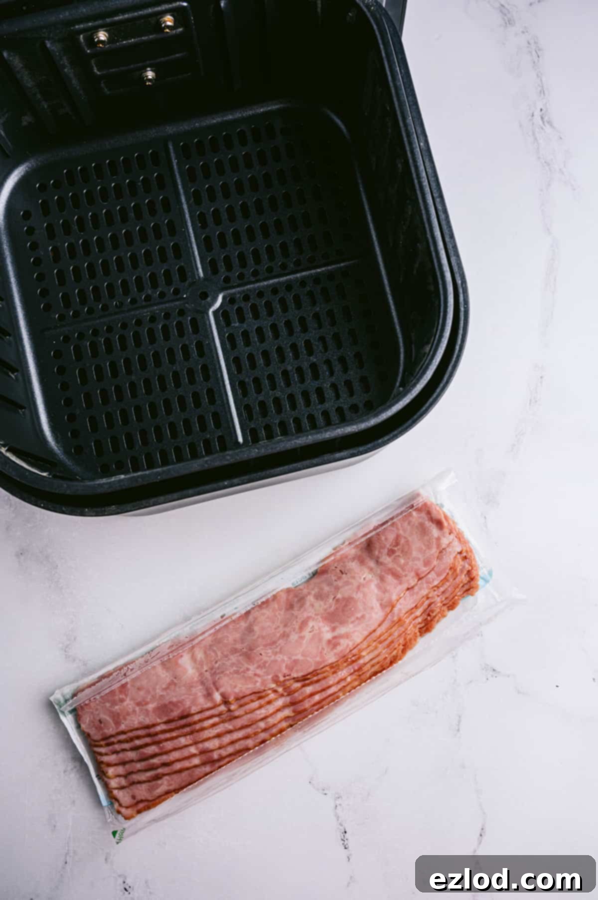 Crispy Air Fryer Turkey Bacon 3 An empty air fryer basket and a package of Turkey Bacon sitting on a marble table.