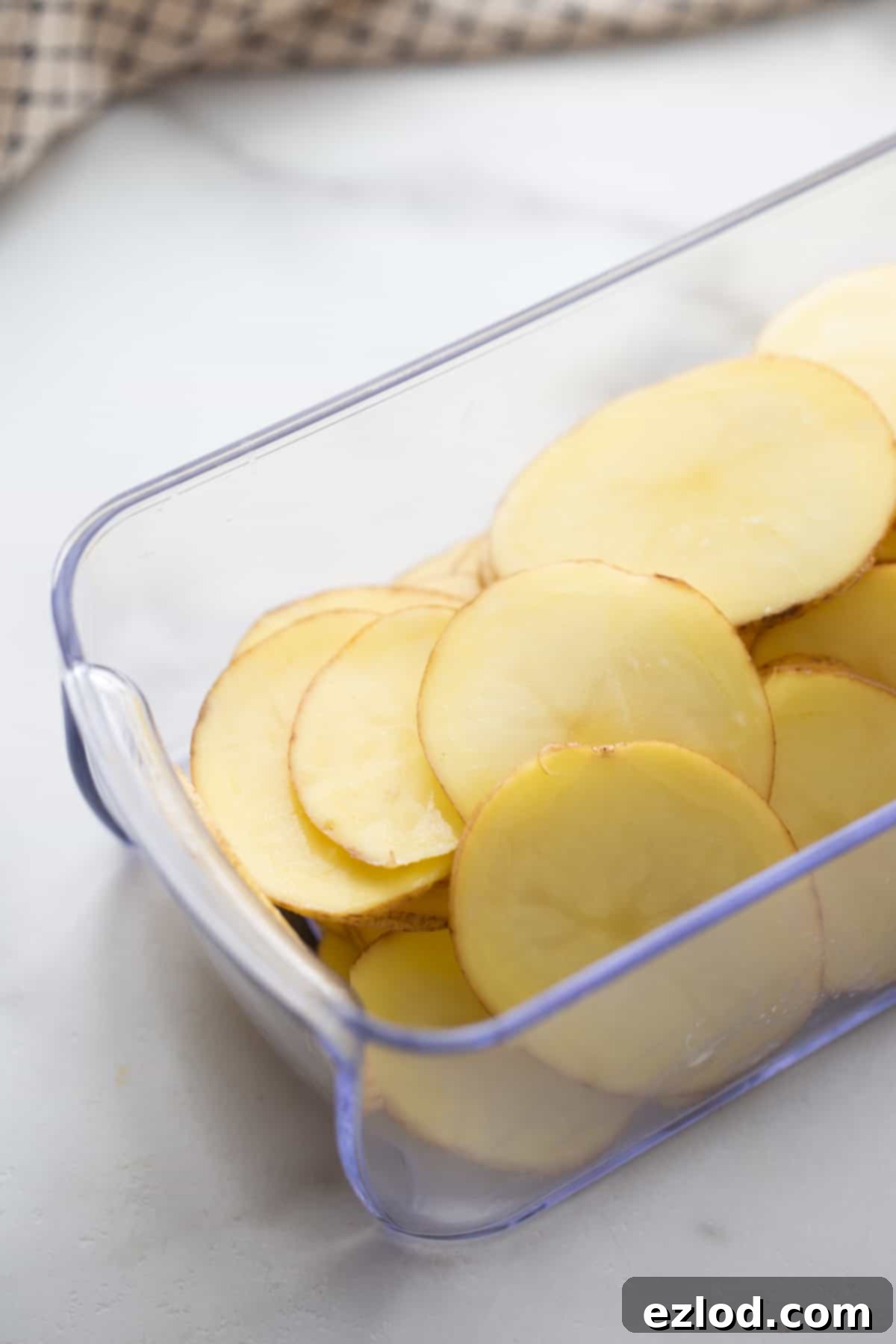 Raw potato being sliced thinly with a mandoline slicer, demonstrating the first step for preparing homemade air fryer potato chips.