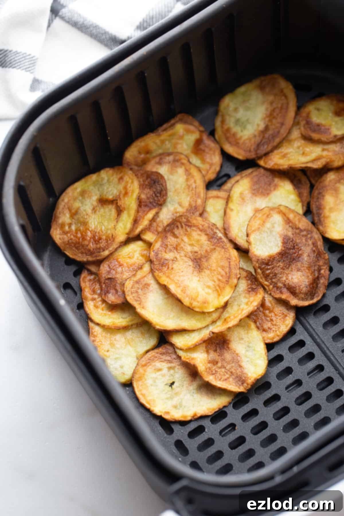 Air fryer basket filled with a single layer of potato chips, halfway through the cooking process.