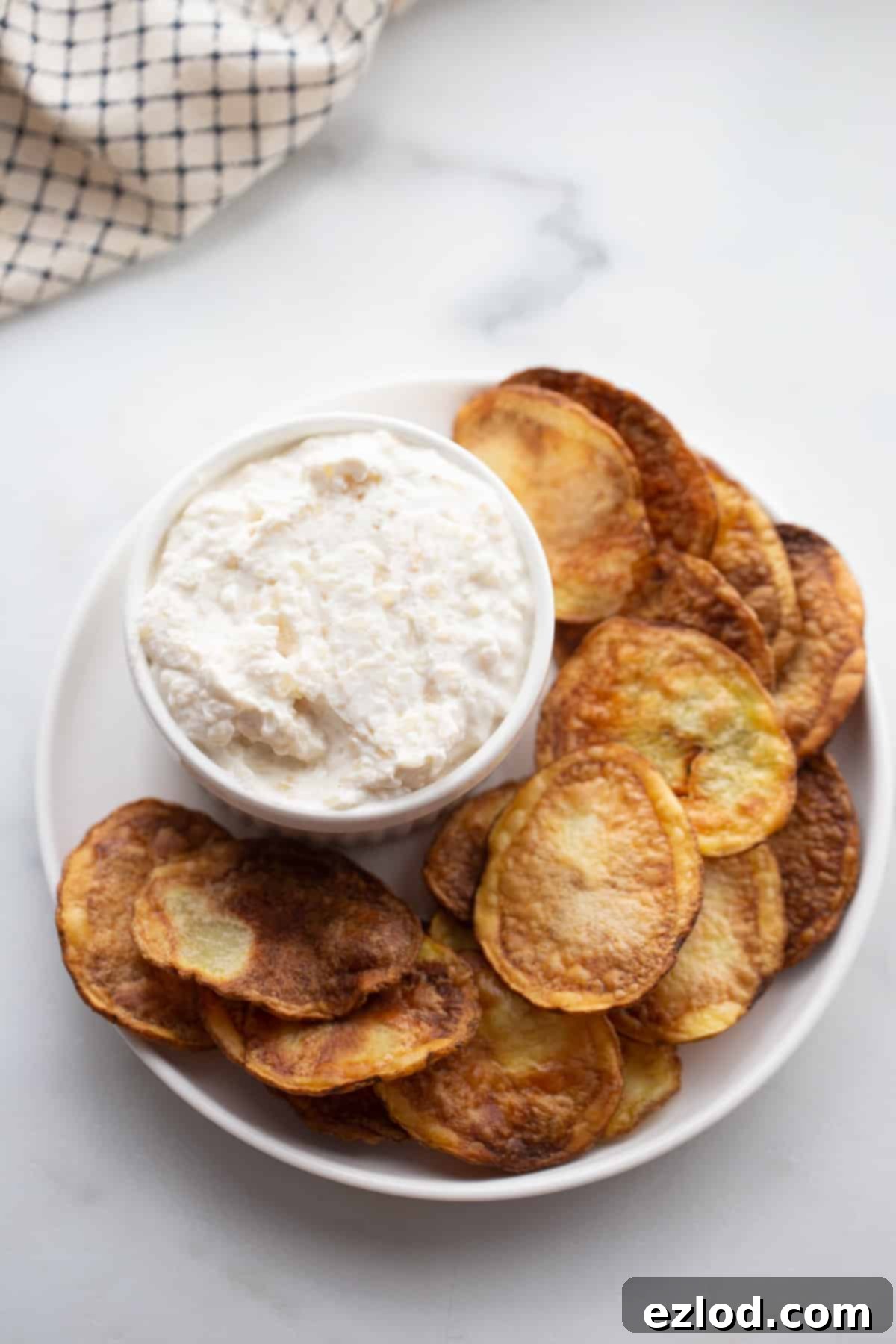 Freshly cooked, golden air fryer potato chips being carefully removed from the air fryer basket with tongs.