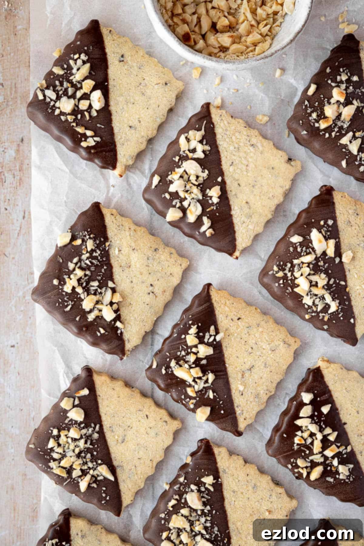 Vegan hazelnut shortbread on a sheet of baking parchment with a bowl of chopped hazelnuts.