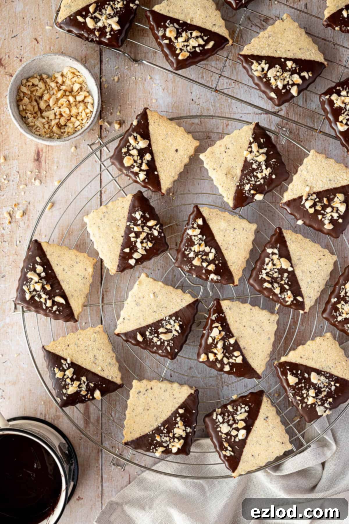 Vegan hazelnut shortbread on wire cooling racks with a mug of melted chocolate and a bowl of chopped hazelnuts.
