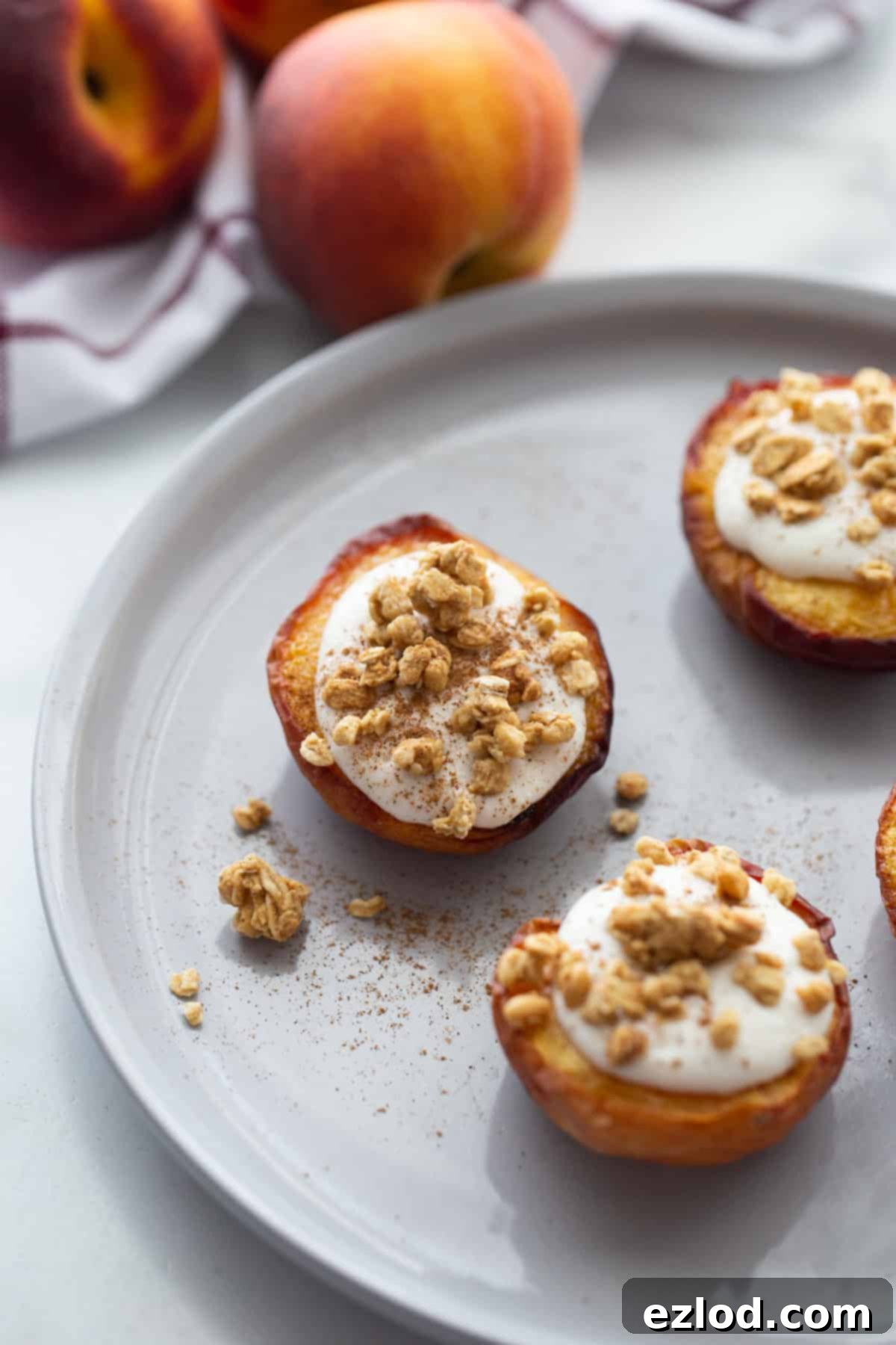 Sweet Air Fried Peaches with Creamy Ricotta 2 Three air fried peach halves on a white plate topped with whipped ricotta, cinnamon, and granola