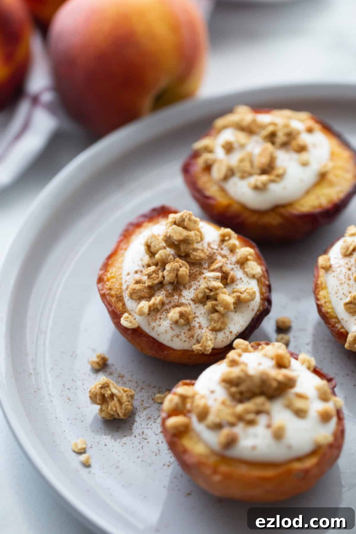 Sweet Air Fried Peaches with Creamy Ricotta 8 Three air fried peach halves on a white plate topped with whipped ricotta cinnamon and granola