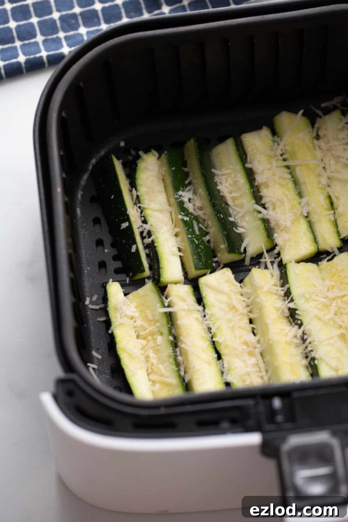 Sliced zucchini arranged in one layer inside of an air fryer basket and topped with shredded parmesan cheese