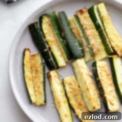 A white plate with air fryer zucchini topped with crispy cheese