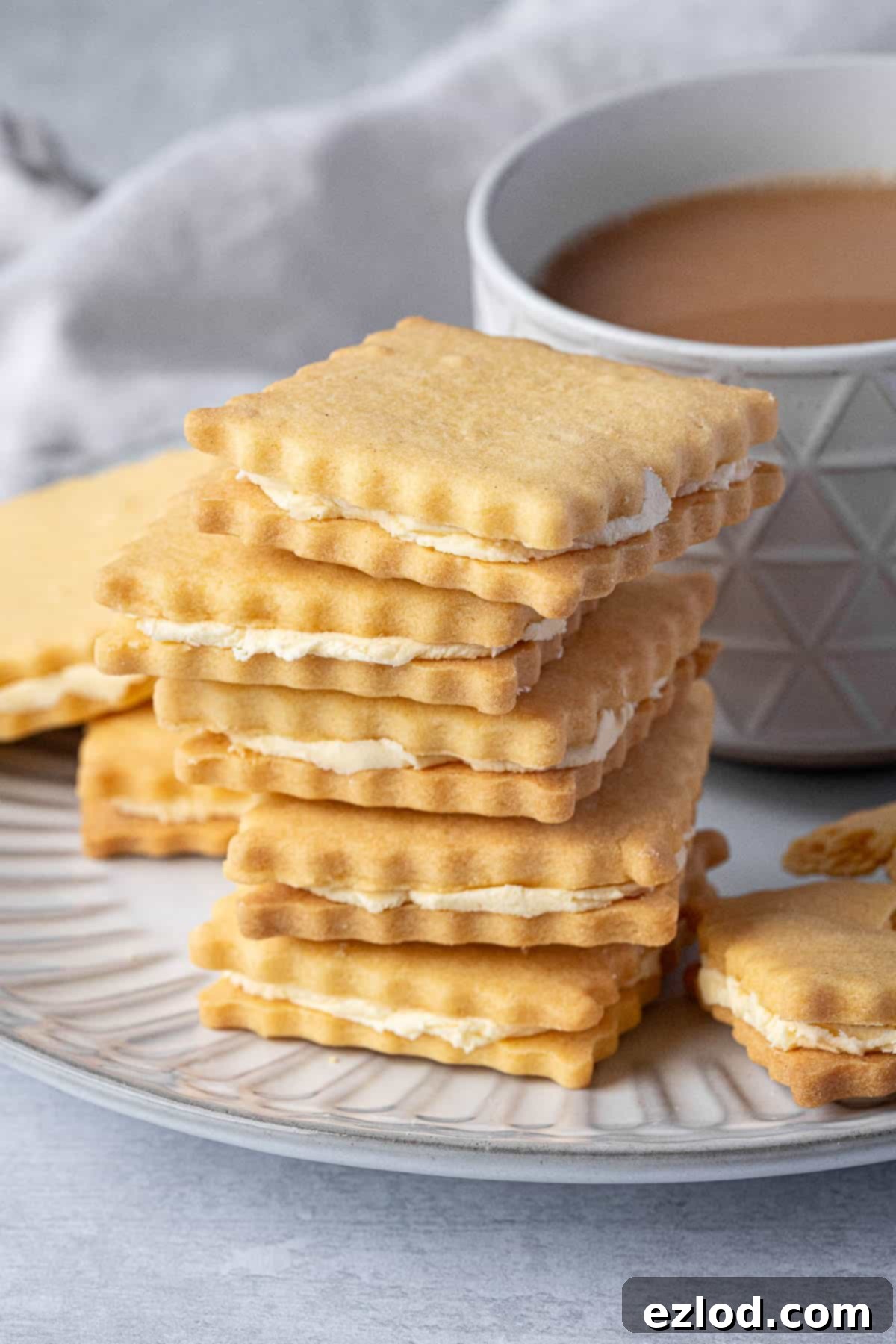 A stack of perfectly golden vegan custard cream biscuits with a steaming cup of tea in the background, inviting a moment of calm.