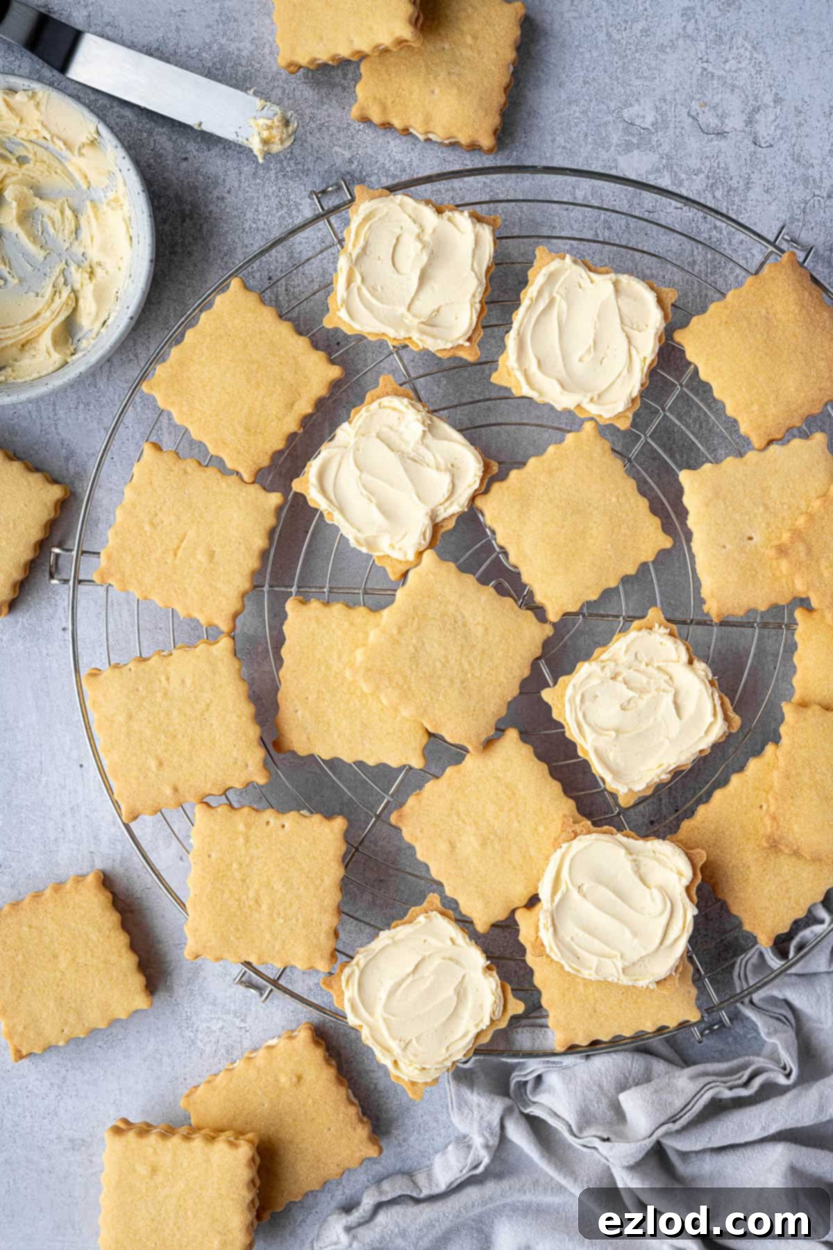 Several freshly assembled vegan custard creams resting on a round wire cooling rack, with a bowl of leftover buttercream nearby.