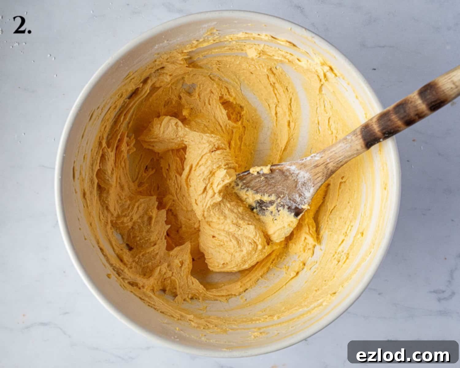 Step 2 in making vegan custard creams: the creamed butter mixture after the custard powder has been fully incorporated, displaying a uniform yellow hue.