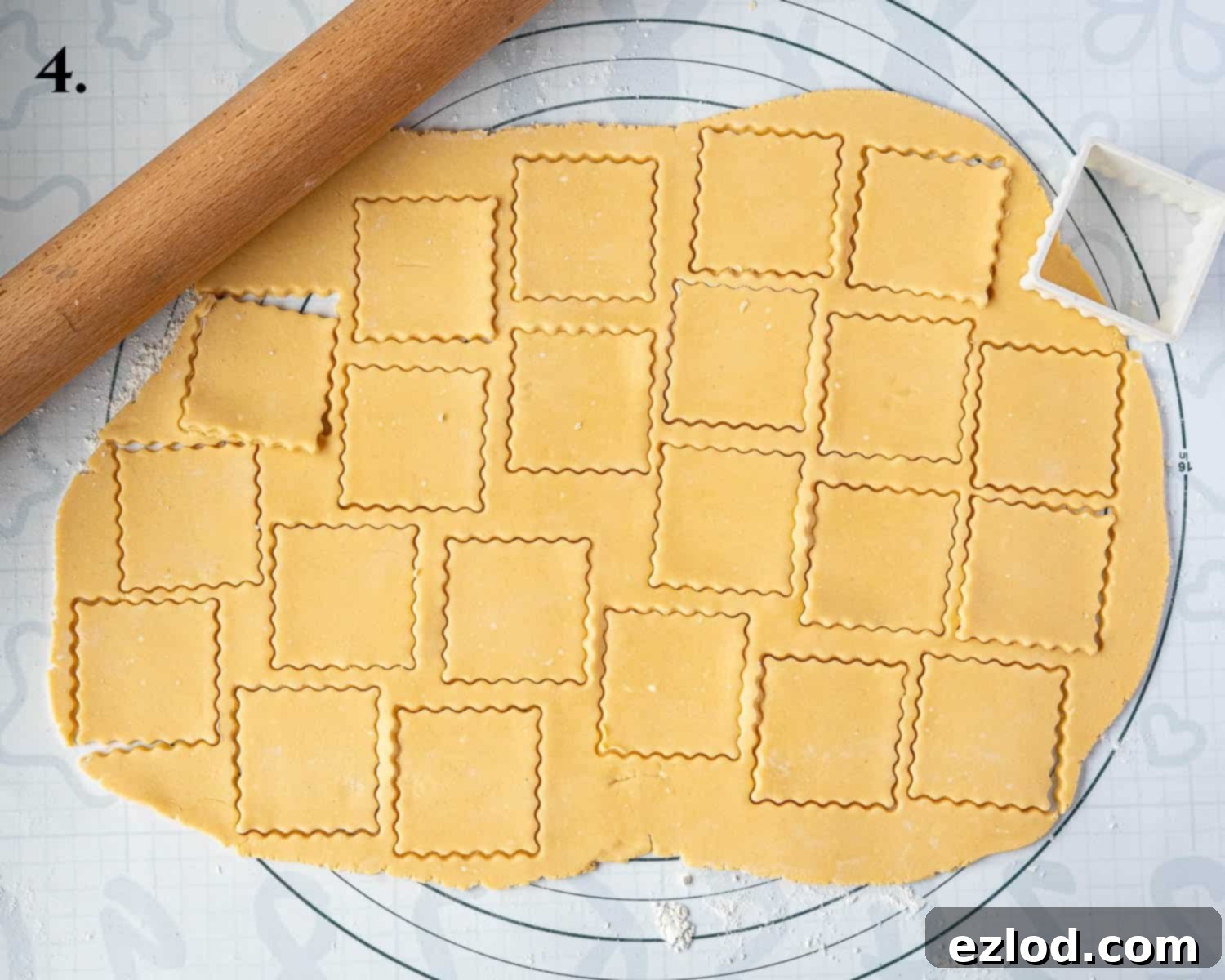 Step 4 in making vegan custard creams: the biscuit dough rolled out on a floured surface, with multiple square shapes already cut out.