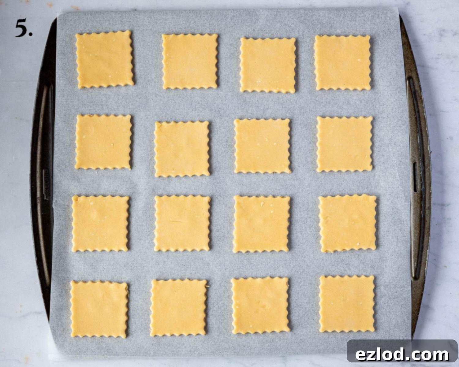 Step 5 in making vegan custard creams: raw biscuit cut-outs neatly arranged and spaced on a parchment-lined baking sheet, prepared for chilling.