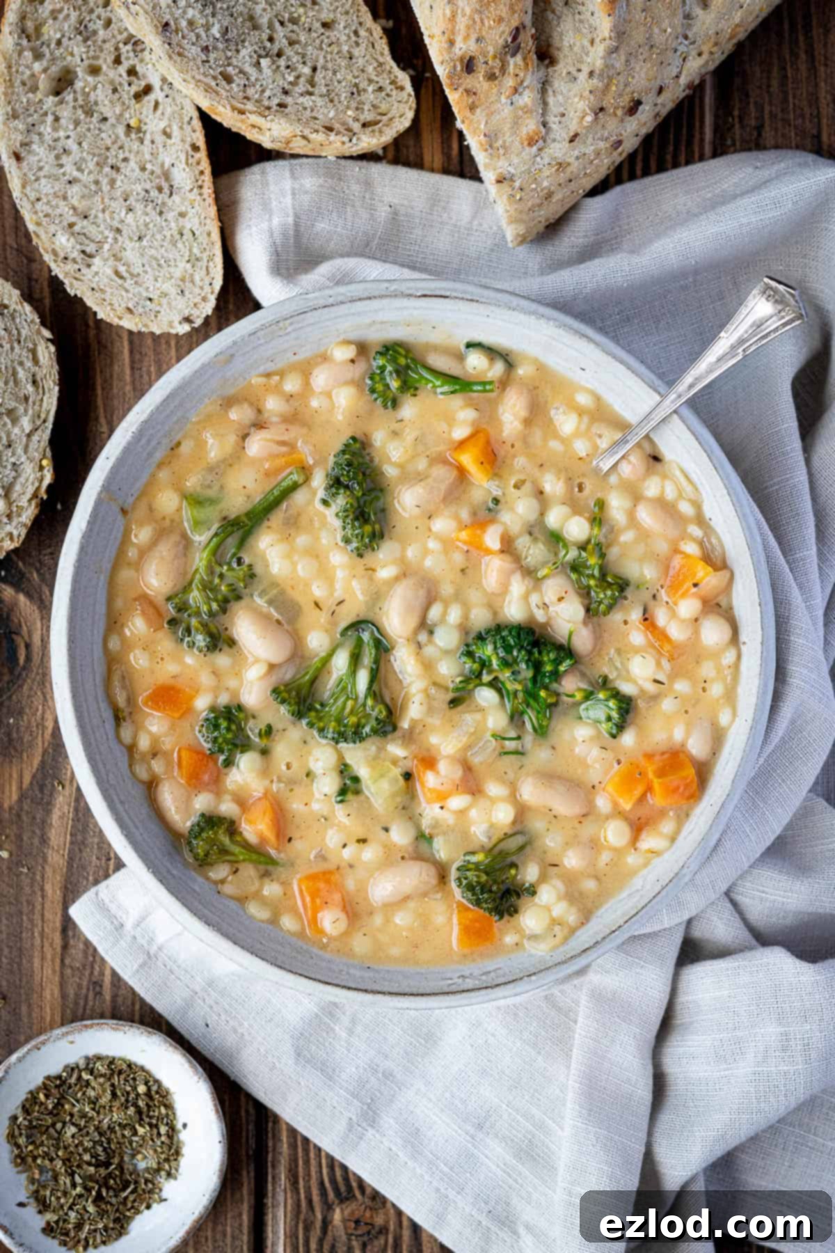 Velvety Vegan Pearl Couscous Soup 2 A bowl of creamy pearl couscous soup on a wooden table with a sliced loaf of bread, showcasing its rich texture and inviting warmth.
