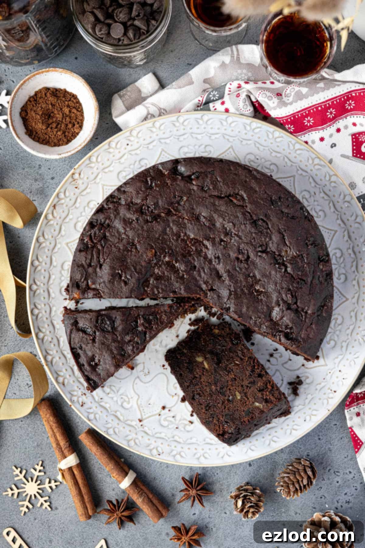 The sliced vegan chocolate Christmas cake on a white plate surrounded by whole spices and wooden Christmas decorations.