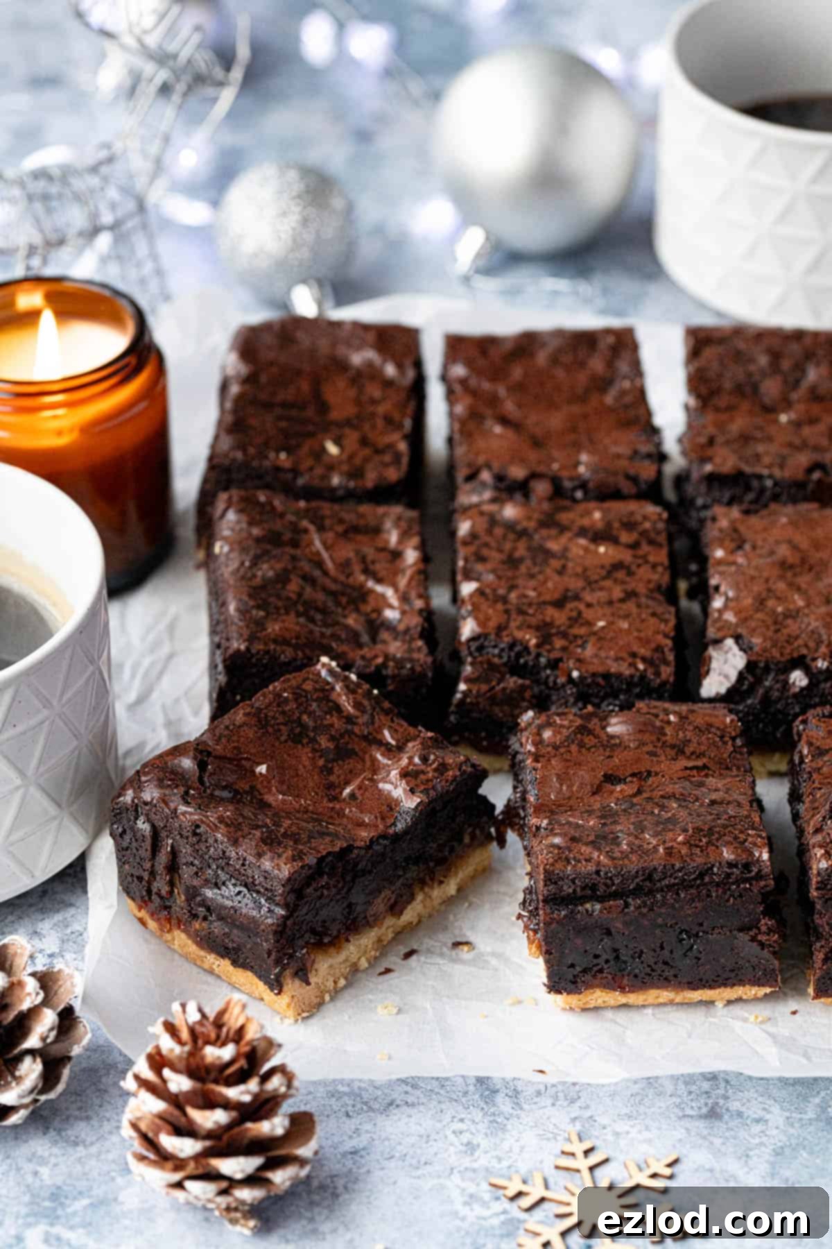 Festive Vegan Mince Pie Brownies 2 Mince pie brownies on a sheet of baking paper with mugs of coffee, candles and Christmas decorations.