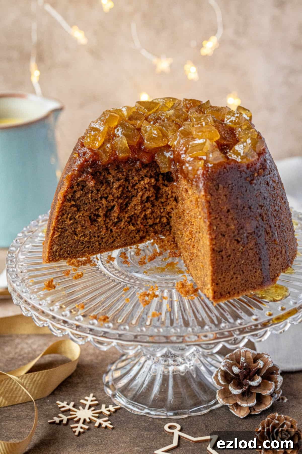 The sliced vegan gingerbread pudding on a glass cake stand with festive lights and decorations, ready to be served.