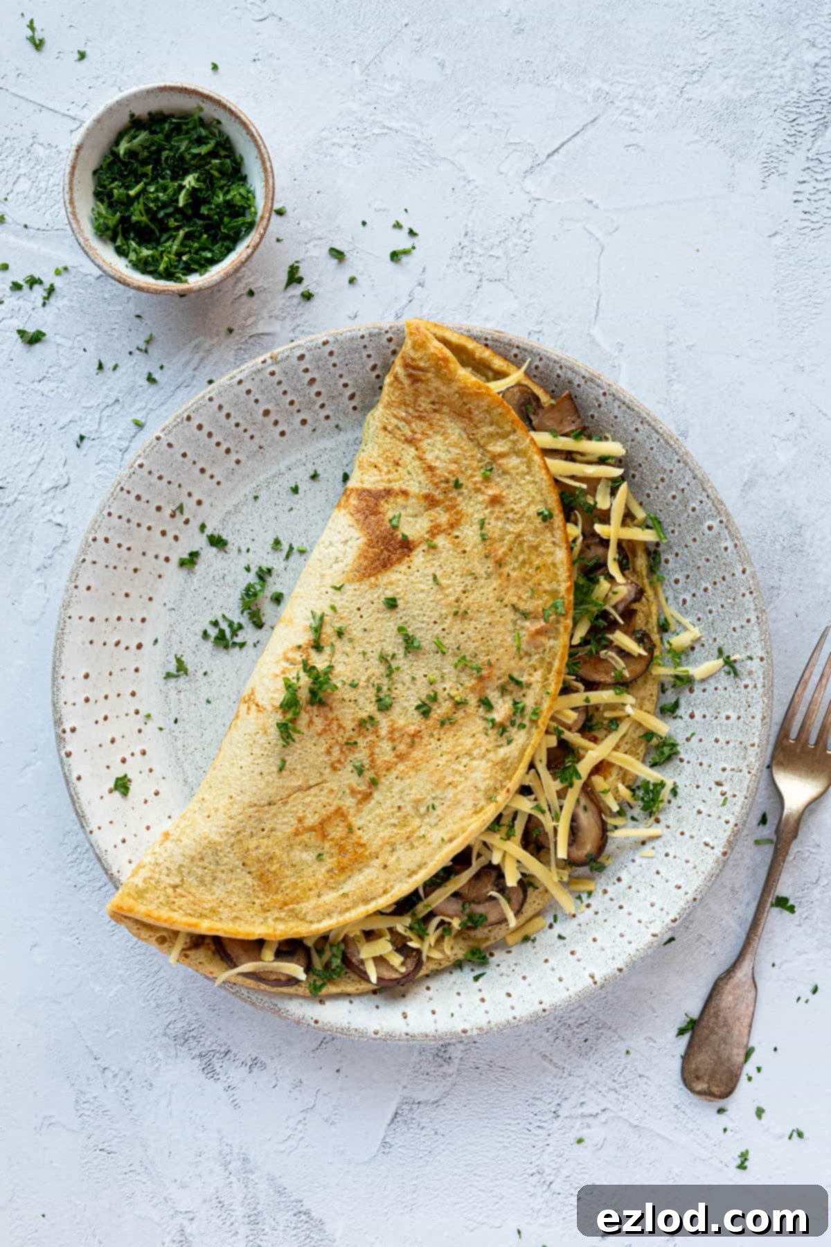 Golden Chickpea Fritters 2 Savoury chickpea pancake filled with sautéed mushrooms and melted vegan cheese, garnished with fresh chopped parsley, served on a pristine white plate.
