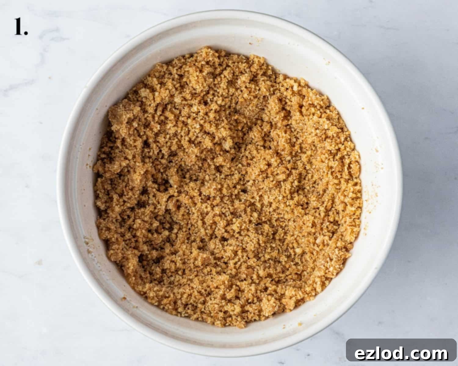 Step 1: Crushed vegan biscuits mixed with melted vegan butter in a bowl, ready for the tart base.