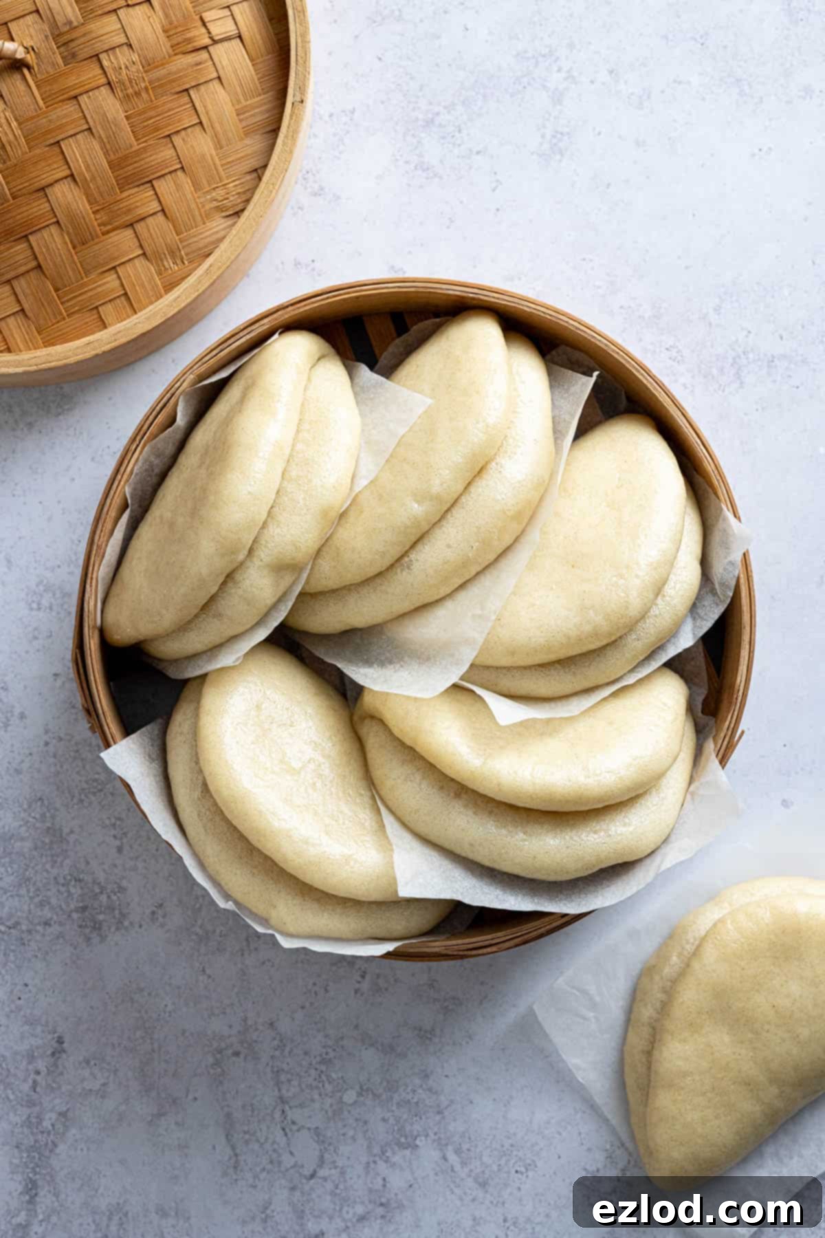 Bao buns on pieces of baking paper in a bamboo steamer, showcasing their soft texture.