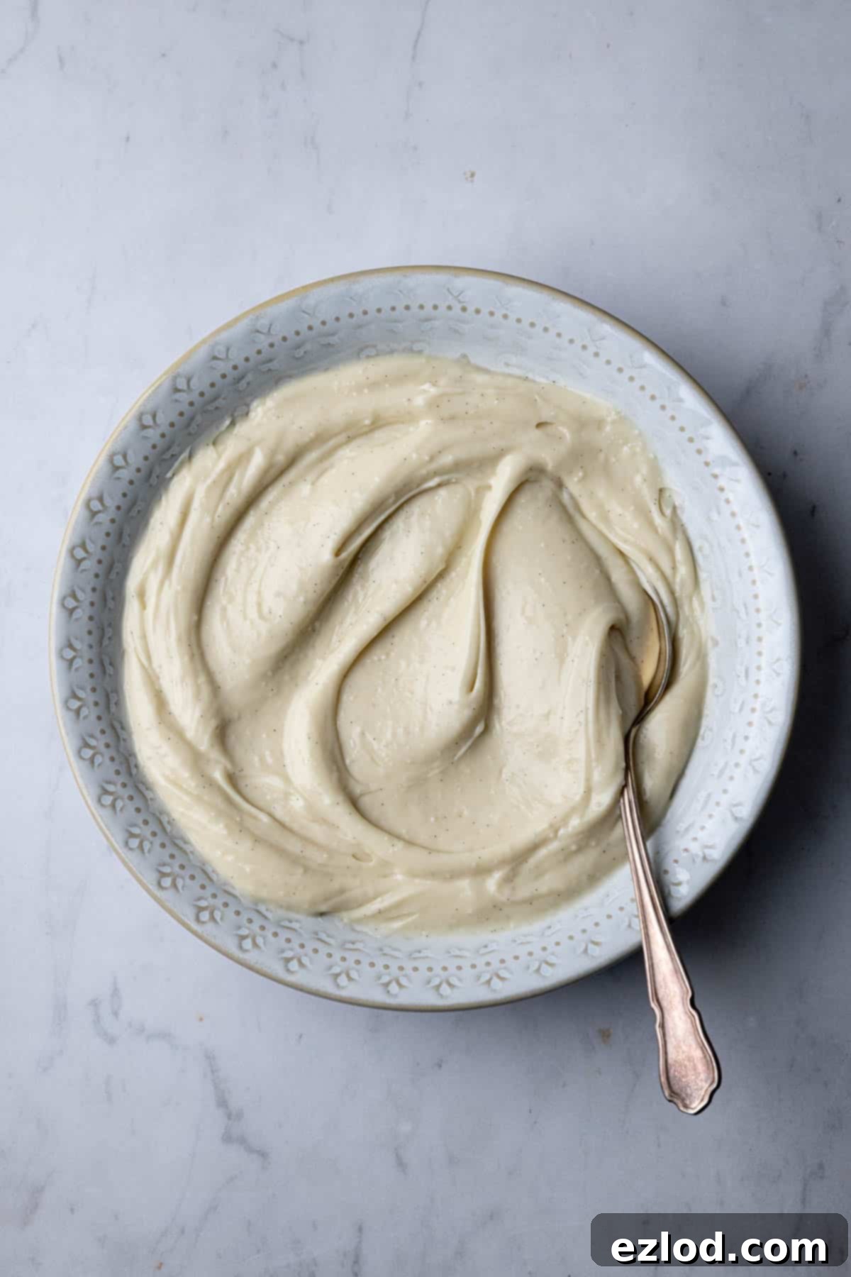 Smooth vegan pastry cream in a white bowl, with a spoon resting inside.